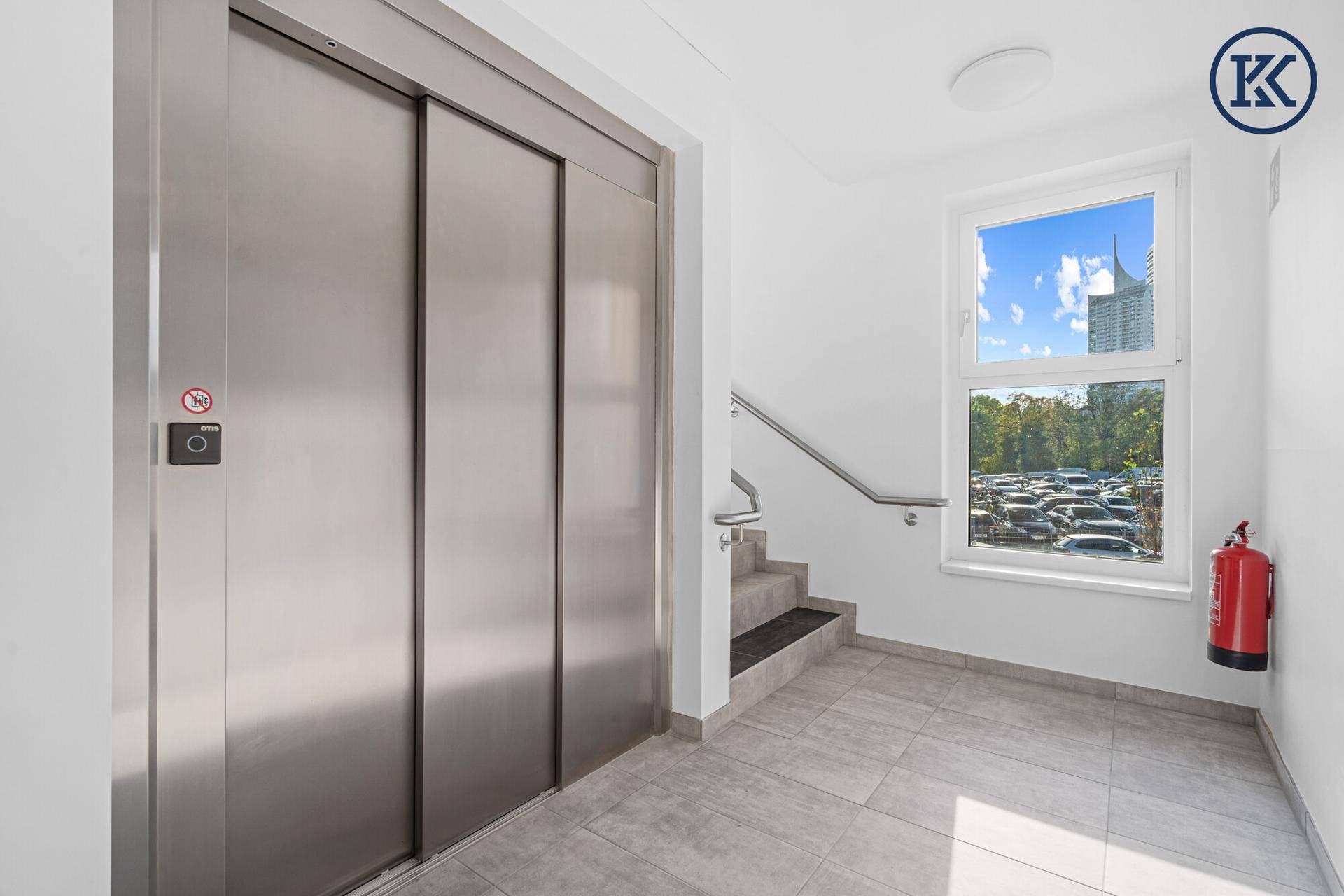 Detailansicht des modernen Aufzugs im hellen Treppenhaus, mit Fenster und Fliesenboden.