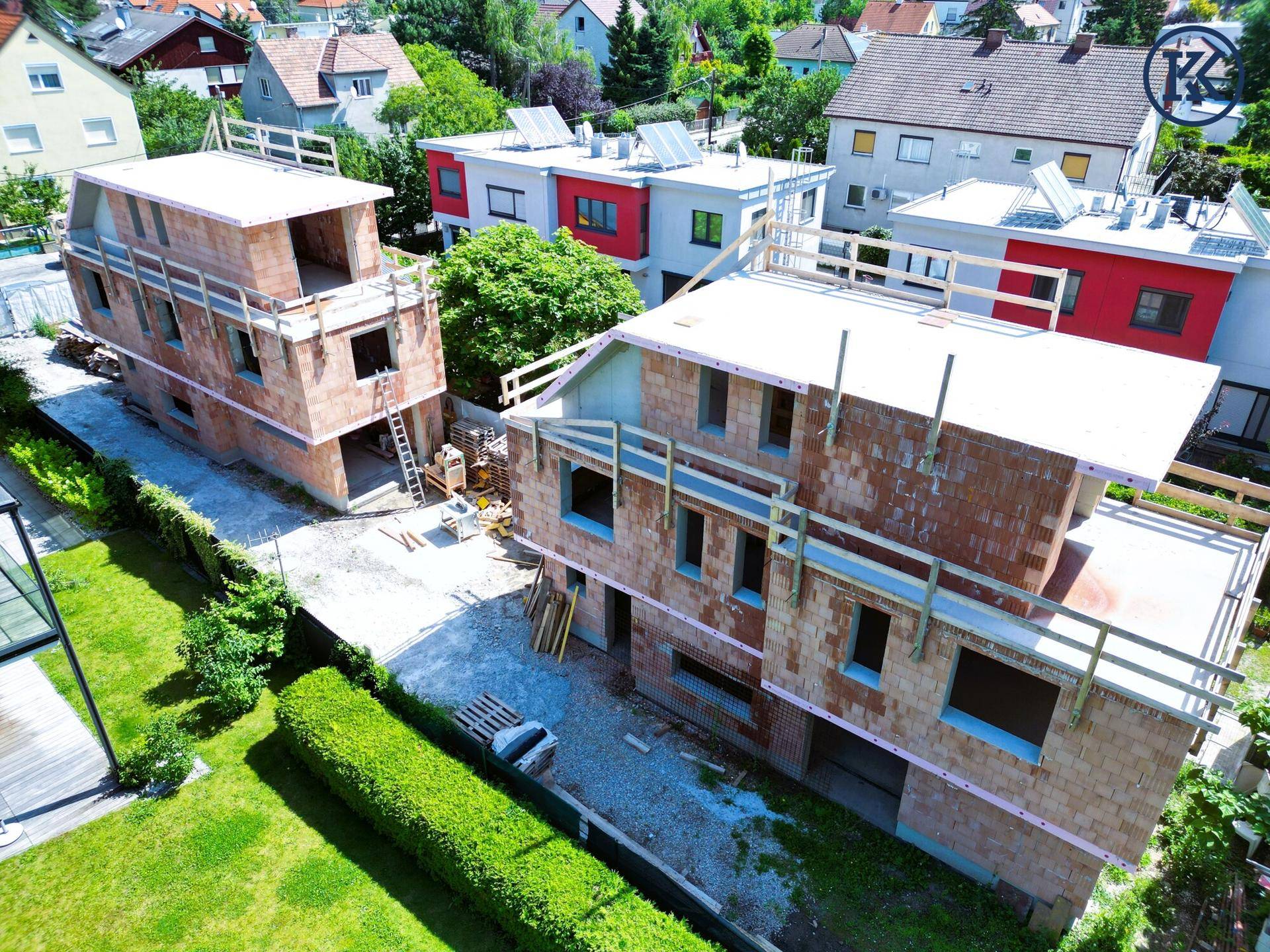 Zwei im Bau befindliche moderne Wohnhäuser mit Flachdächern in einer grünen Wohngegend.