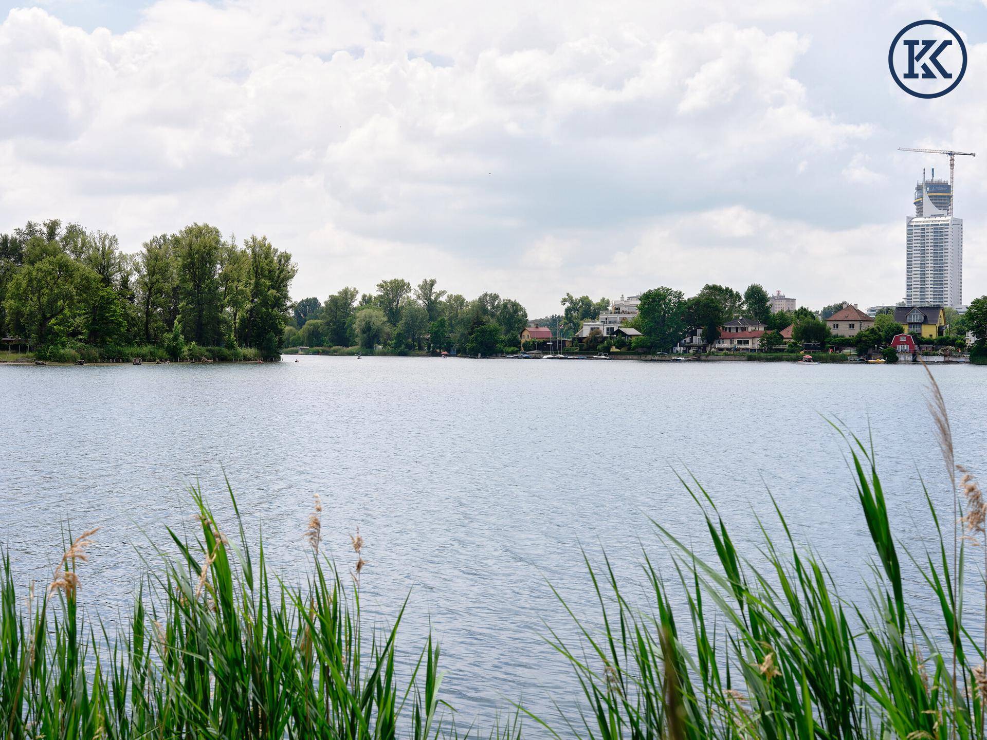 Ruhiger Blick über den See mit grünen Ufern und einer sich entwickelnden Stadtkulisse am Horizont.