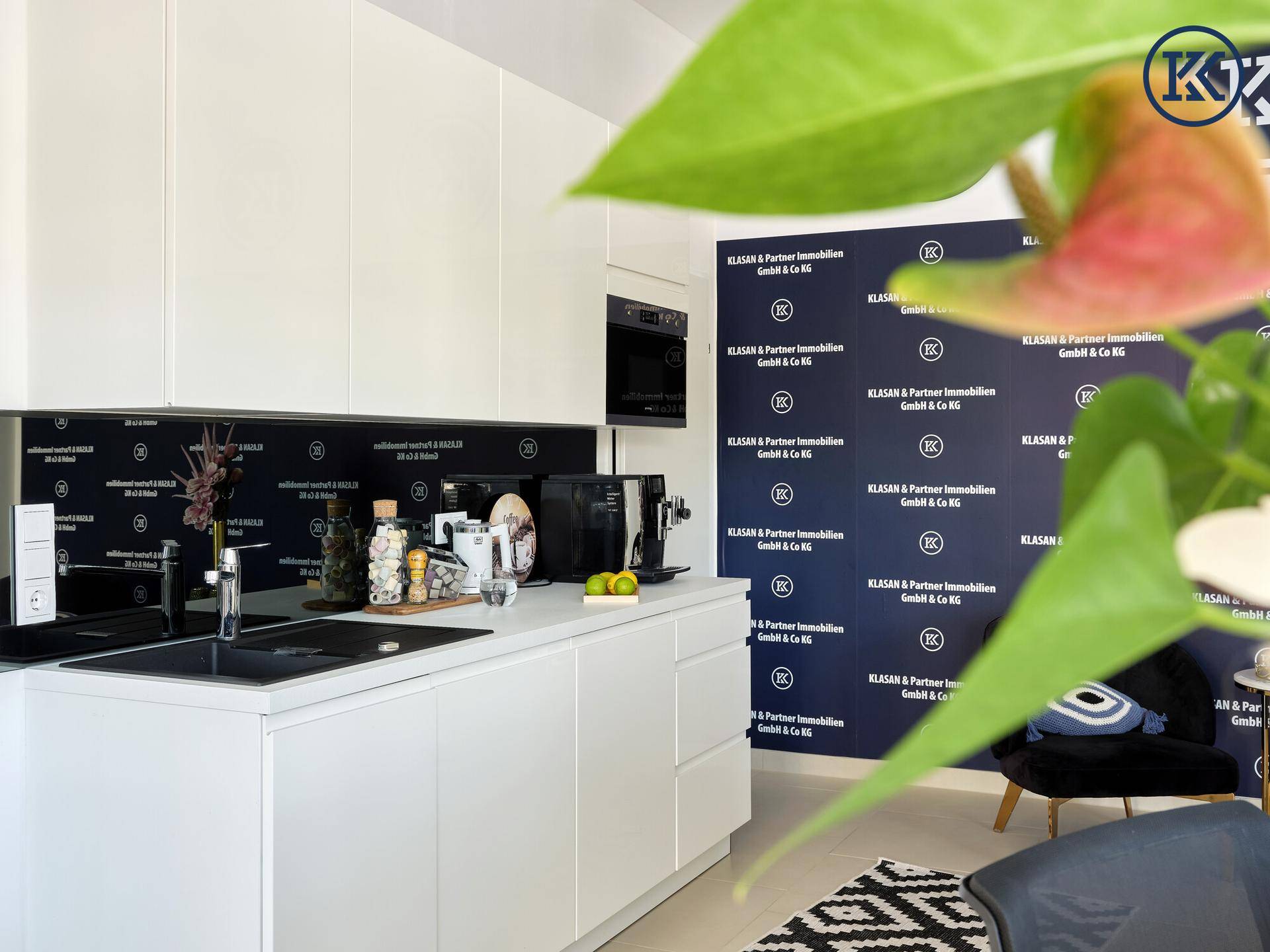Moderne weiße Küchenzeile mit integrierten Geräten und dunkler Rückwand im Büro.