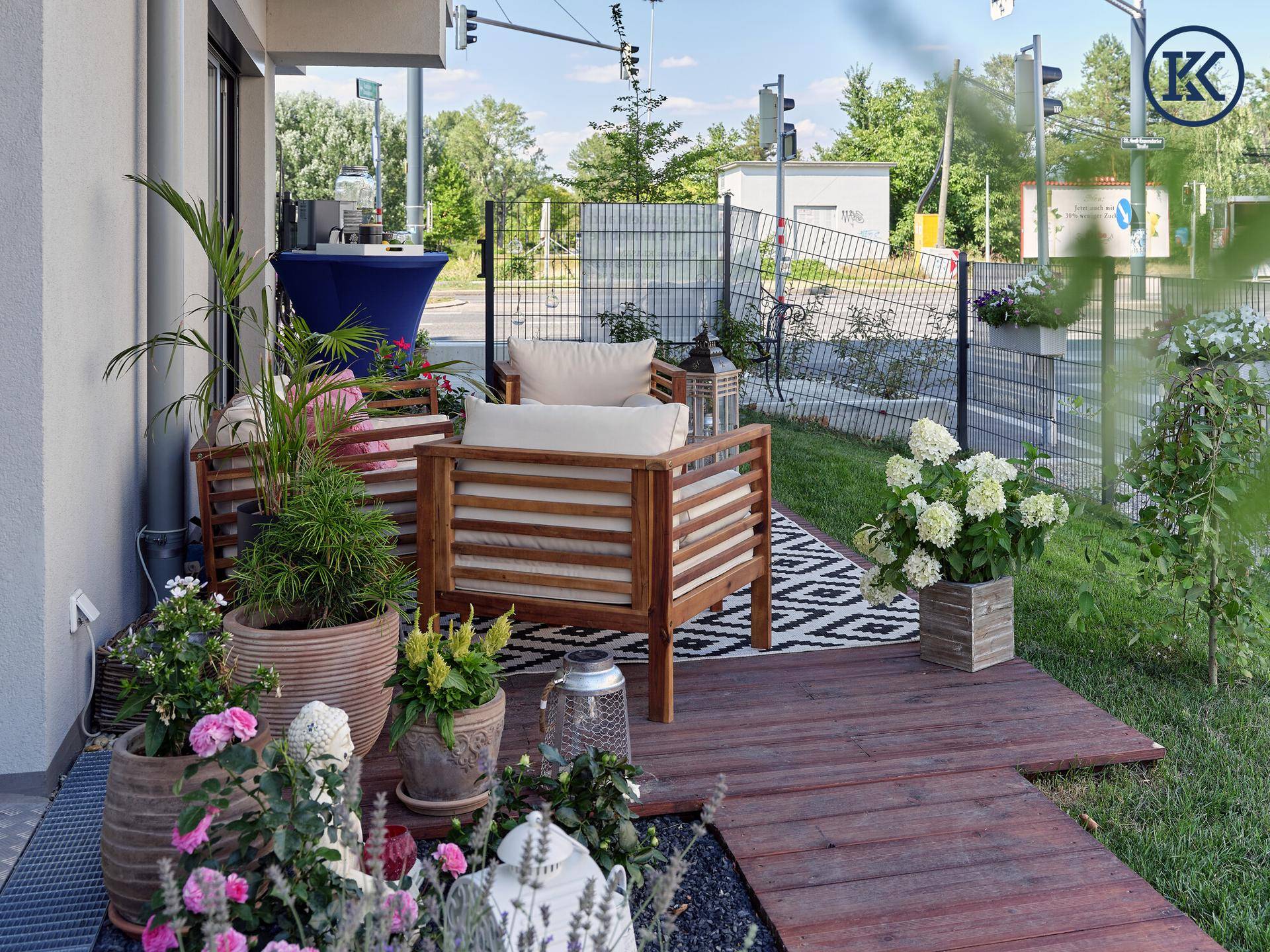 Außenbereich mit Holzterrasse, Gartenmöbeln und üppiger Bepflanzung in der Nähe einer Straße.