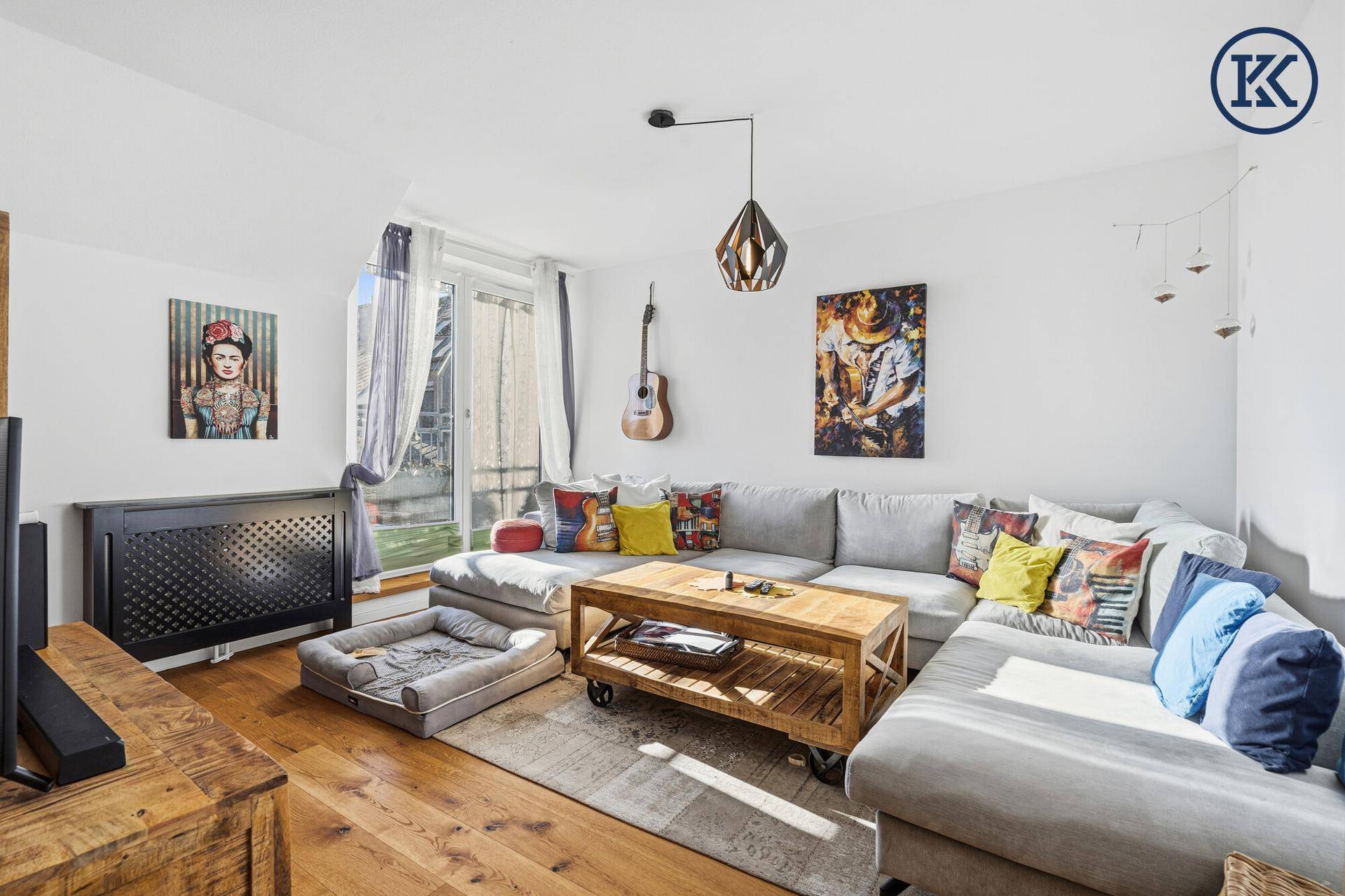 Gemütliches Wohnzimmer mit großem Ecksofa, Holztisch und farbenfrohen Kunstwerken an den Wänden.