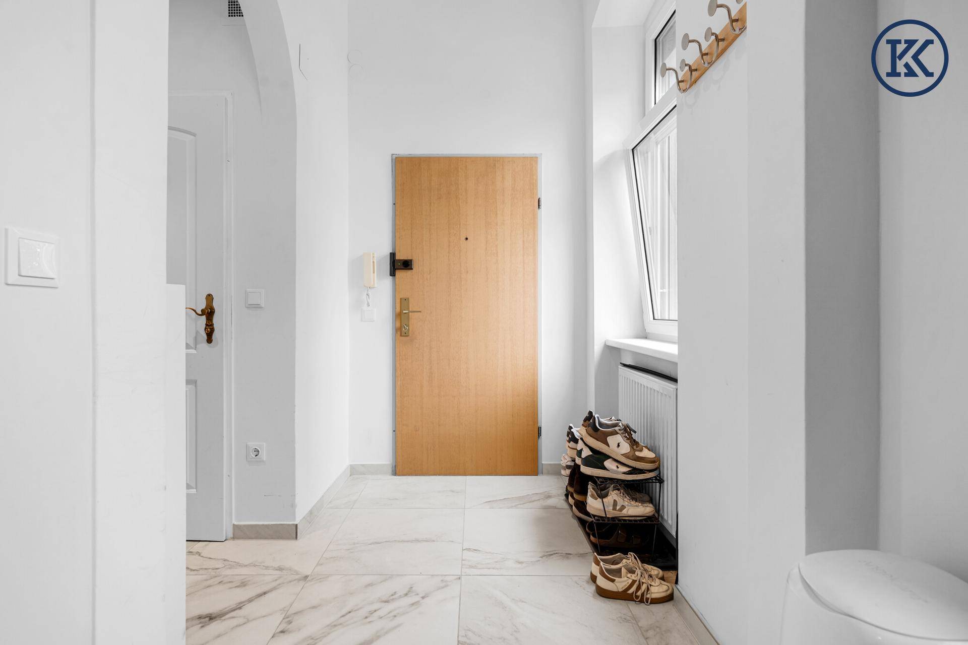 Heller Eingangsbereich mit weißem Marmorfliesenboden, Holztür und einem Fenster für Tageslicht.