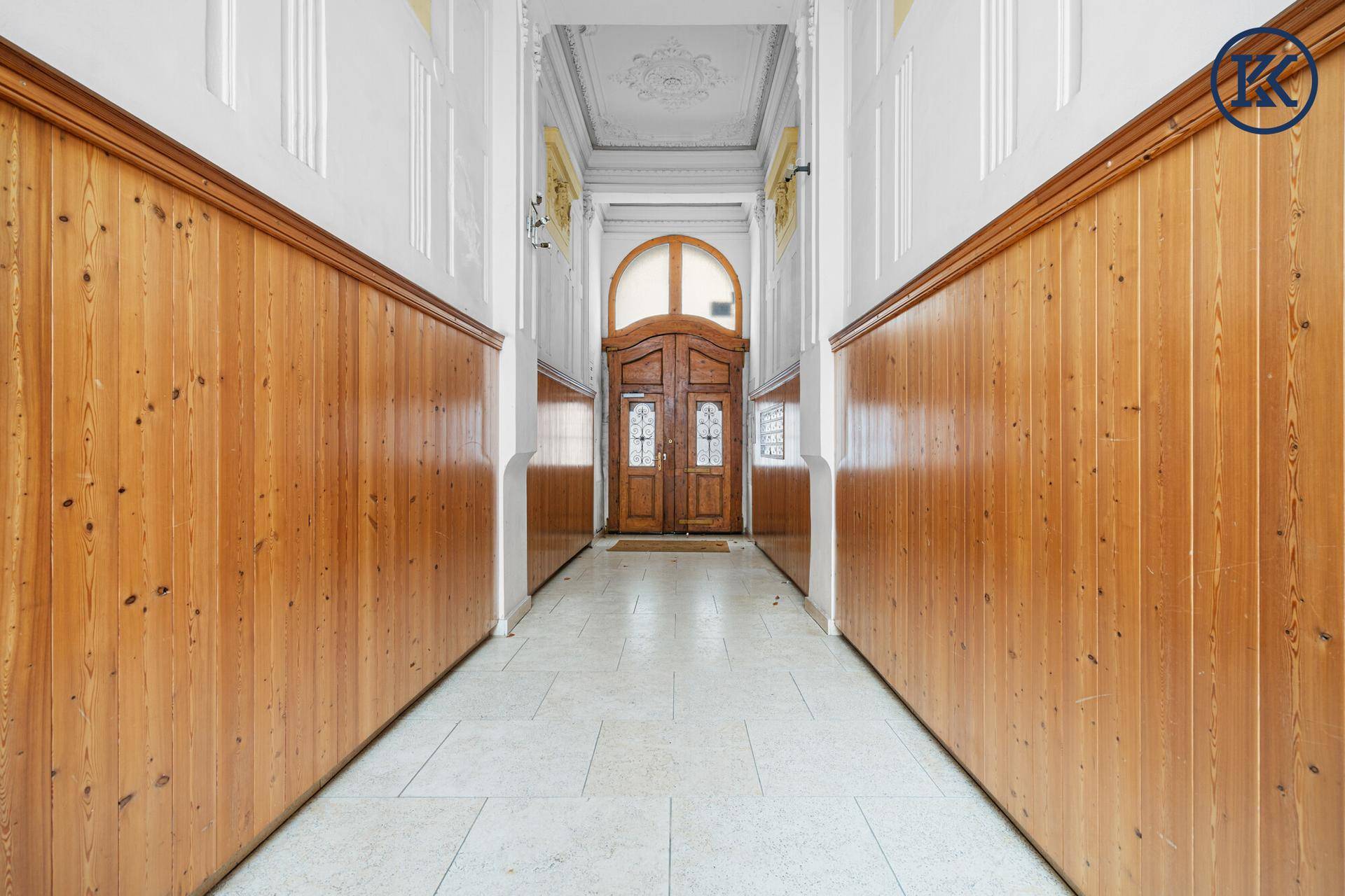 Langer, eleganter Flur mit Holzvertäfelung, Stuckdecke und einer beeindruckenden Holztür am Ende.