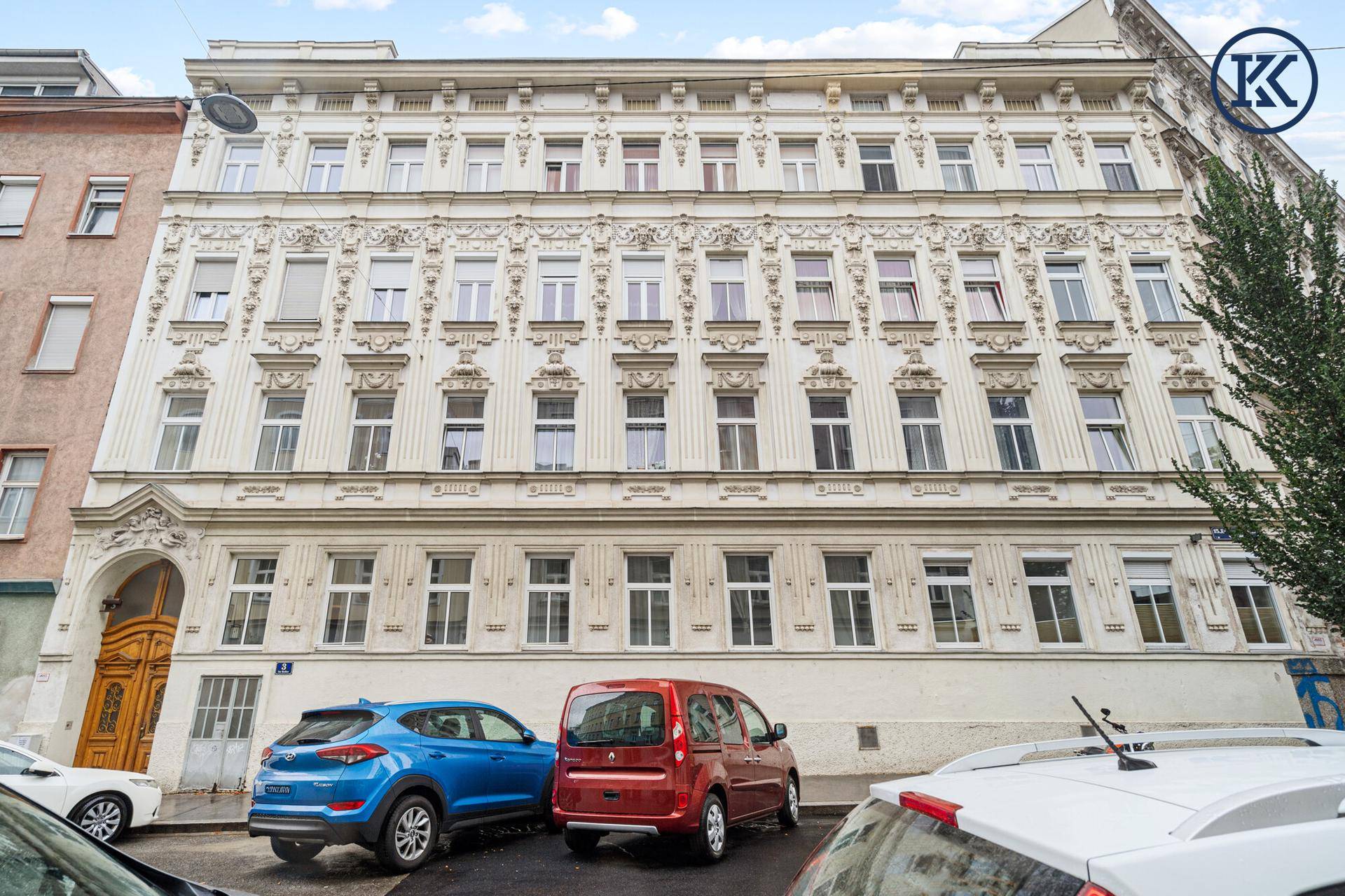 Historische Fassade eines Mehrfamilienhauses mit reich verzierten Details und vielen Fenstern.