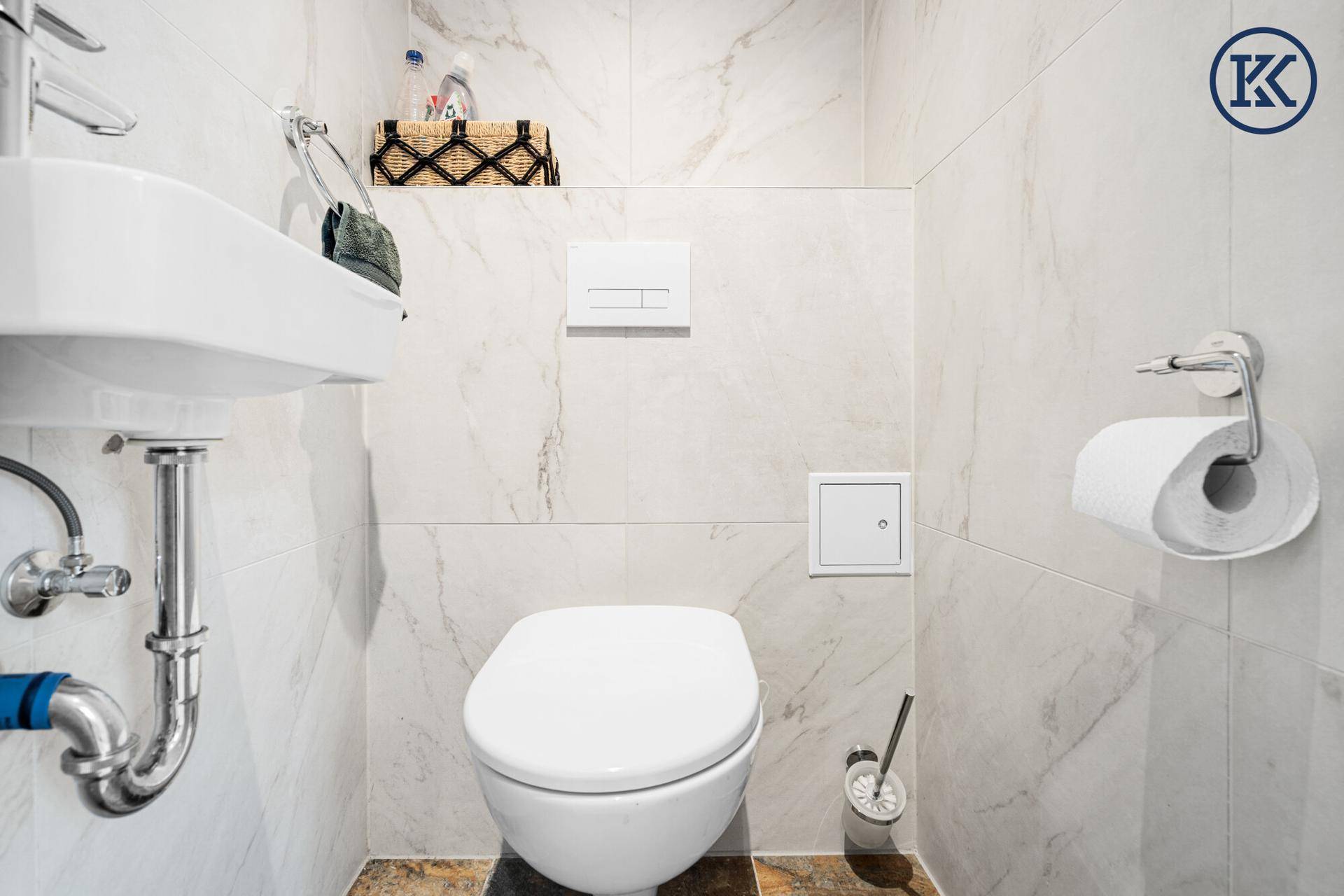 Modernes Gäste-WC mit wandhängender Toilette, kleinem Waschbecken und Marmorfliesen.