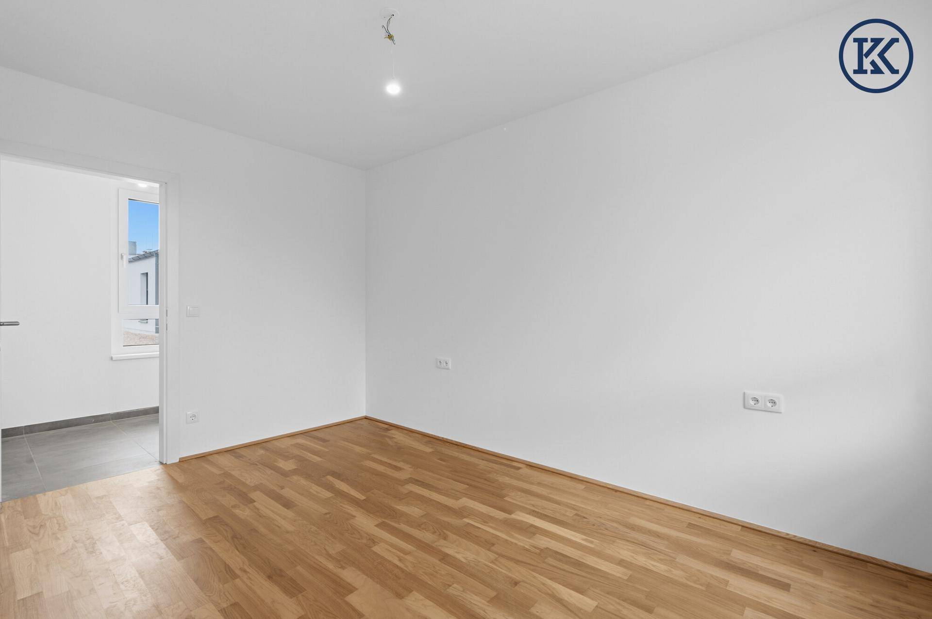 Helles Zimmer mit Parkettboden und Zugang zu einem weiteren Raum.