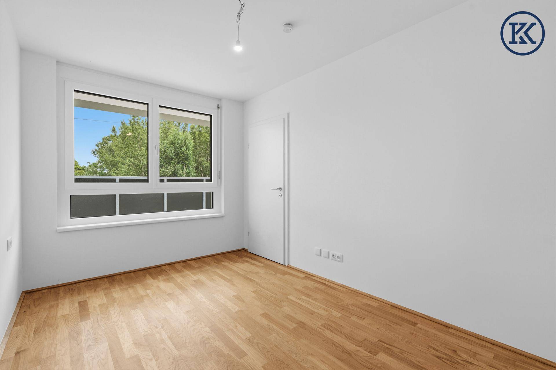 Helles Zimmer mit Parkettboden und großem Fenster mit Ausblick.