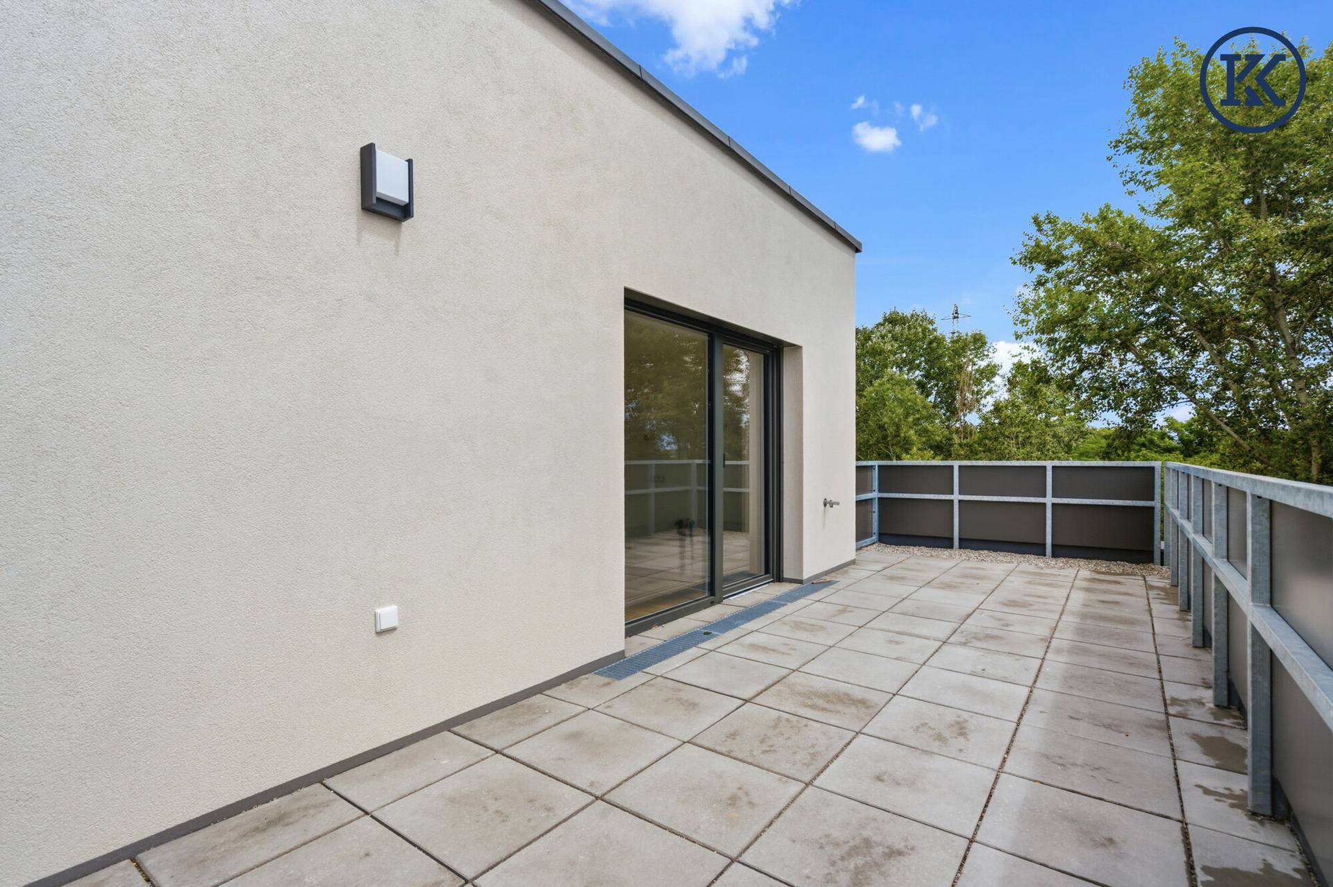 Große, geflieste Terrasse mit Schiebetürzugang und Blick auf Bäume.