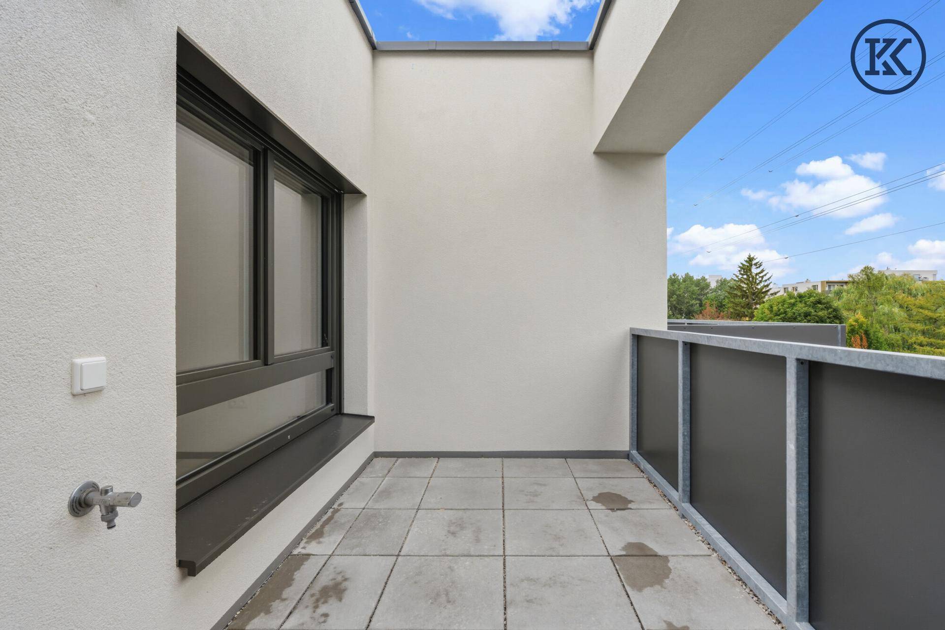 Heller Balkon mit Fliesenboden und Blick auf die Umgebung unter blauem Himmel.