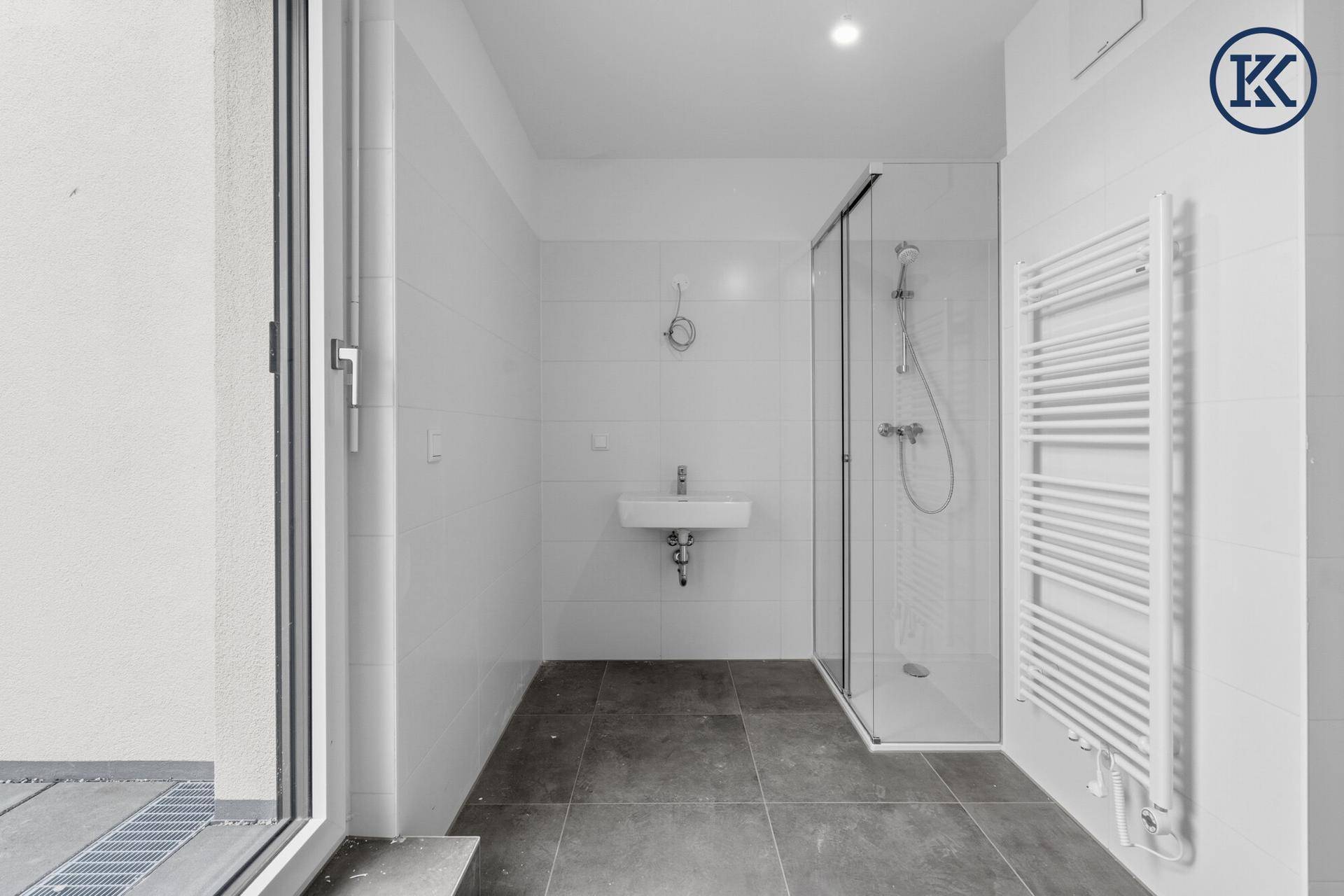 Helles Badezimmer mit Dusche, Waschbecken und Handtuchheizkörper, mit Zugang nach draußen.