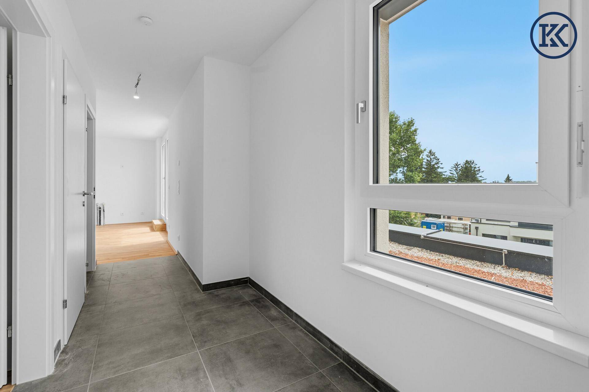 Heller Flur mit Fliesenboden und Blick auf den Außenbereich durch ein großes Fenster.