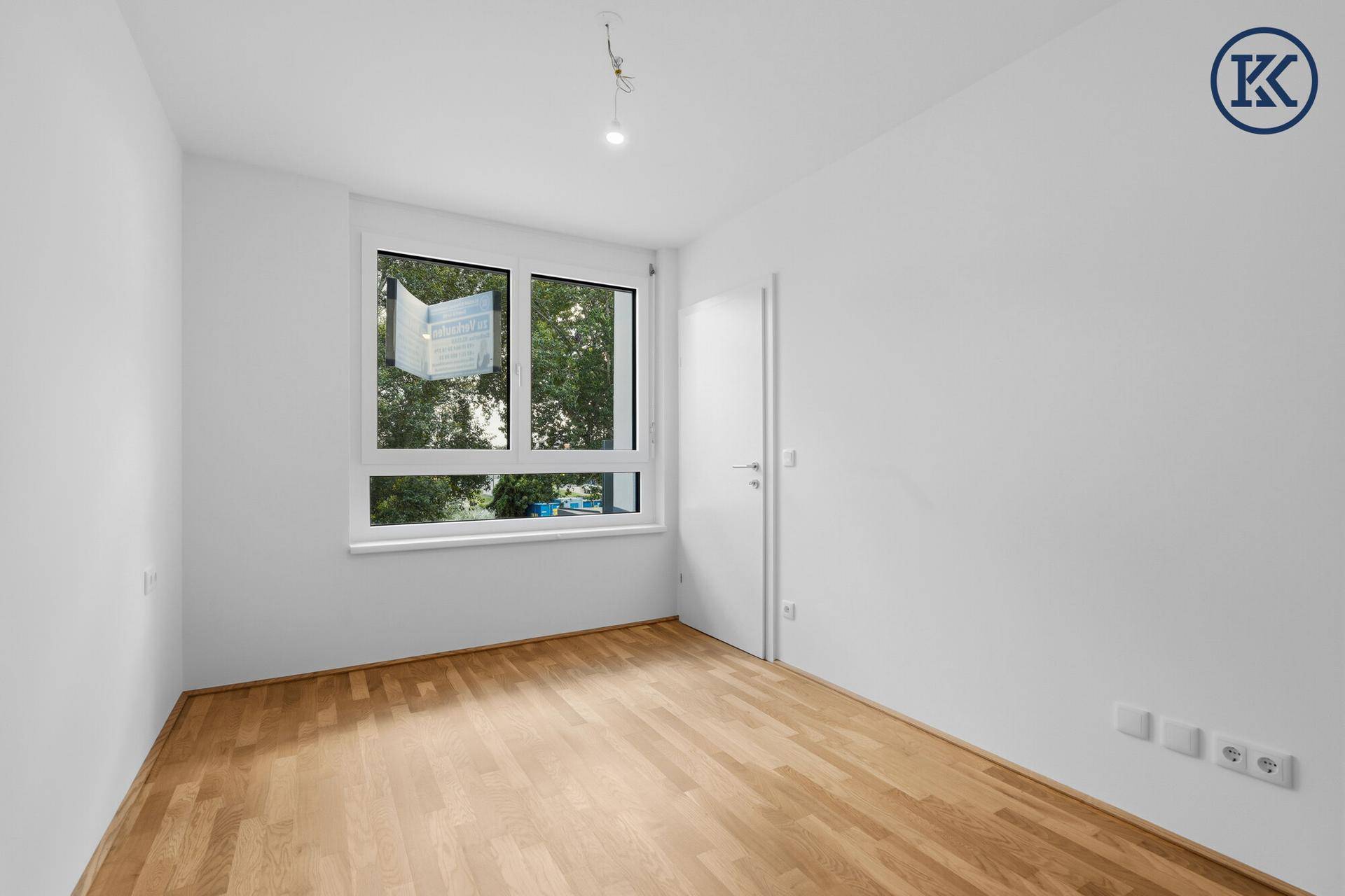 Helles Schlafzimmer mit Parkettboden und Fenster mit Blick ins Grüne.