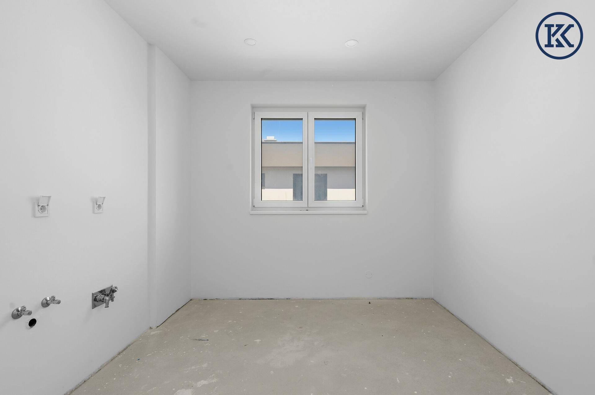 Unmöblierter Raum mit Fenster und Anschlüssen für Sanitärinstallationen, ideal als Hauswirtschaftsraum.