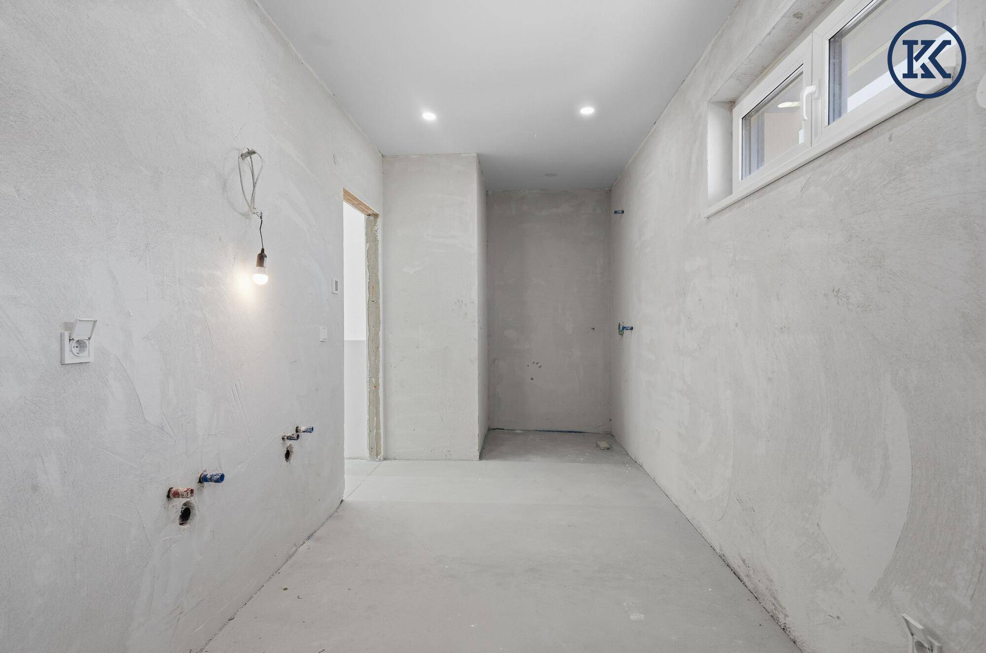 Langer, schmaler Raum im Rohbau mit kleinem Fenster und sichtbaren Leitungen, ideal für Abstellraum.