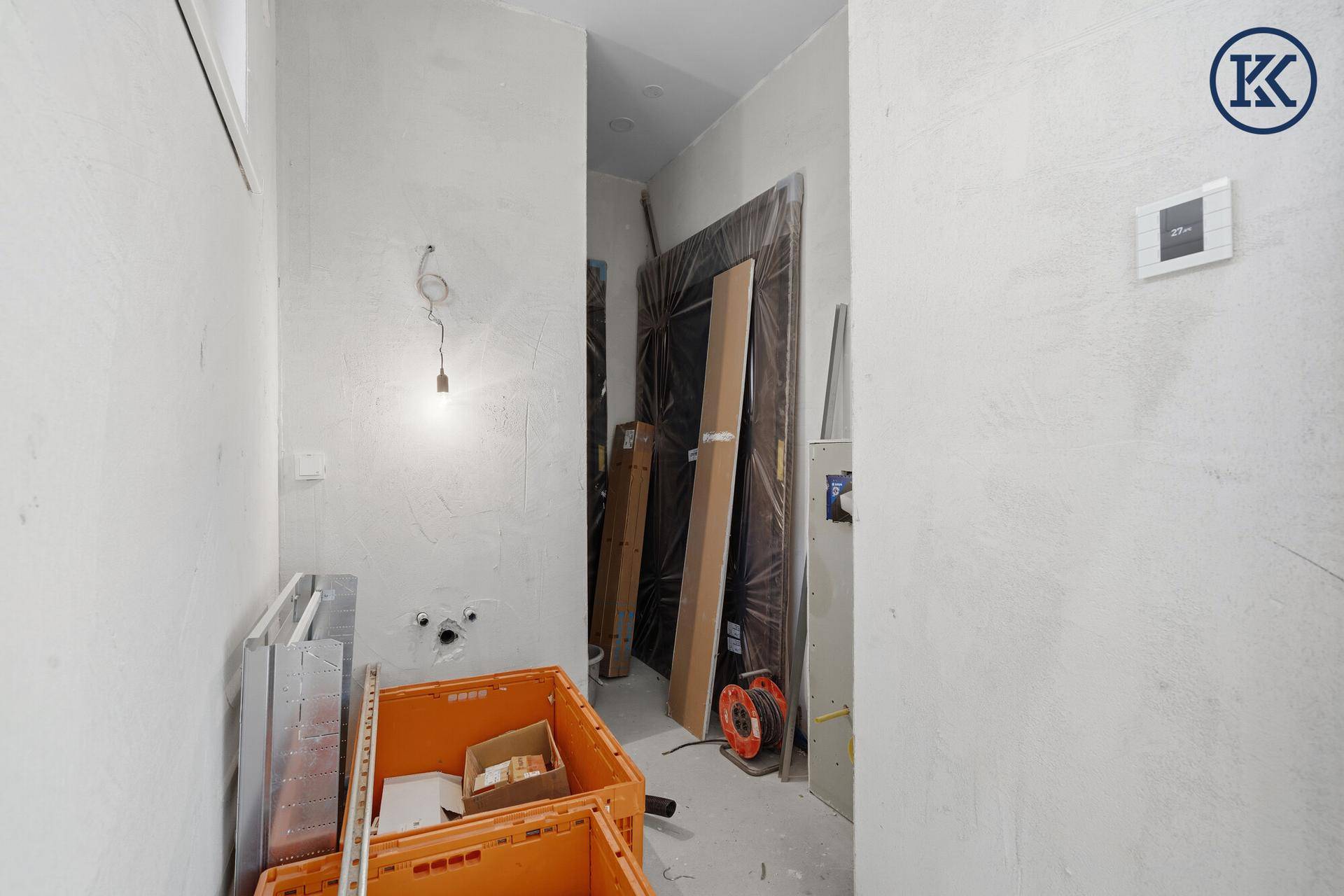 Kleiner Abstellraum im Rohbau mit Baumaterialien und provisorischer Beleuchtung, bereit für den Ausbau.