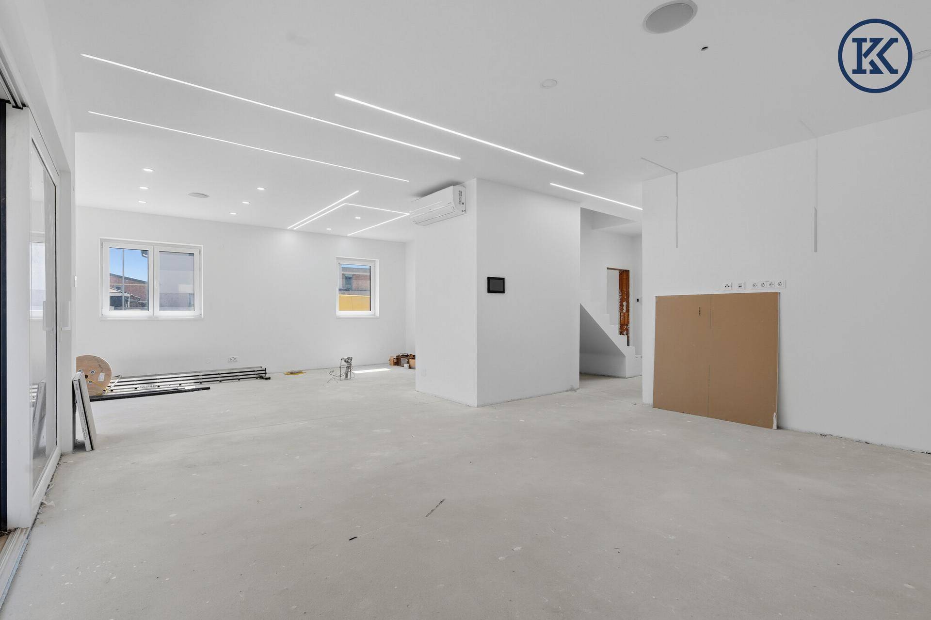 Heller, offener Wohnbereich im Neubau mit großen Fenstern, Klimaanlage und modernen Lichtleisten.