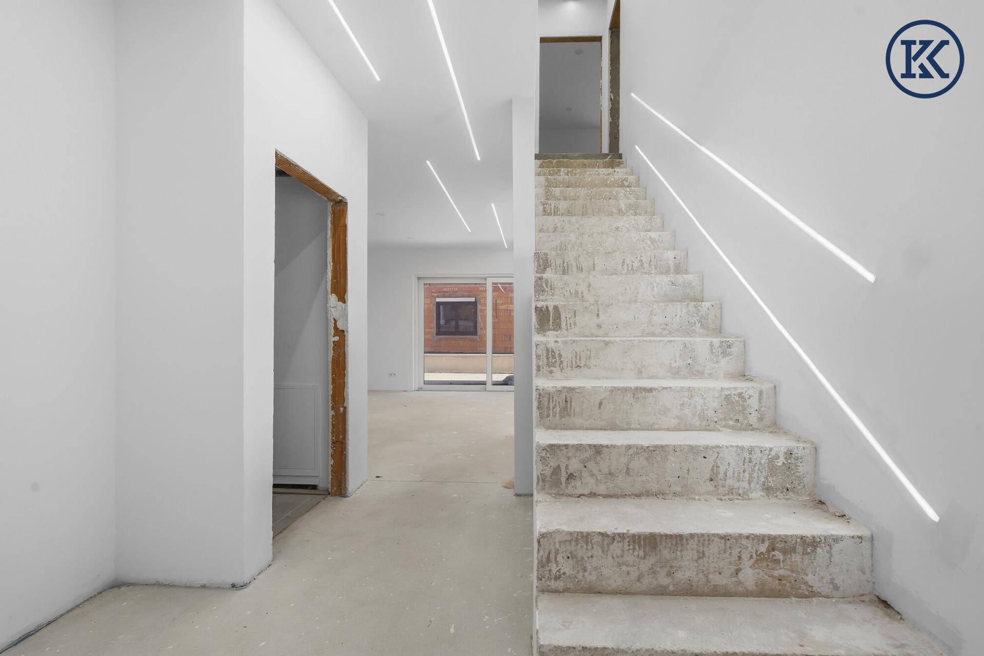 Treppenhaus im Rohbau mit modernen Lichtleisten an der Decke und Blick in den offenen Wohnbereich.