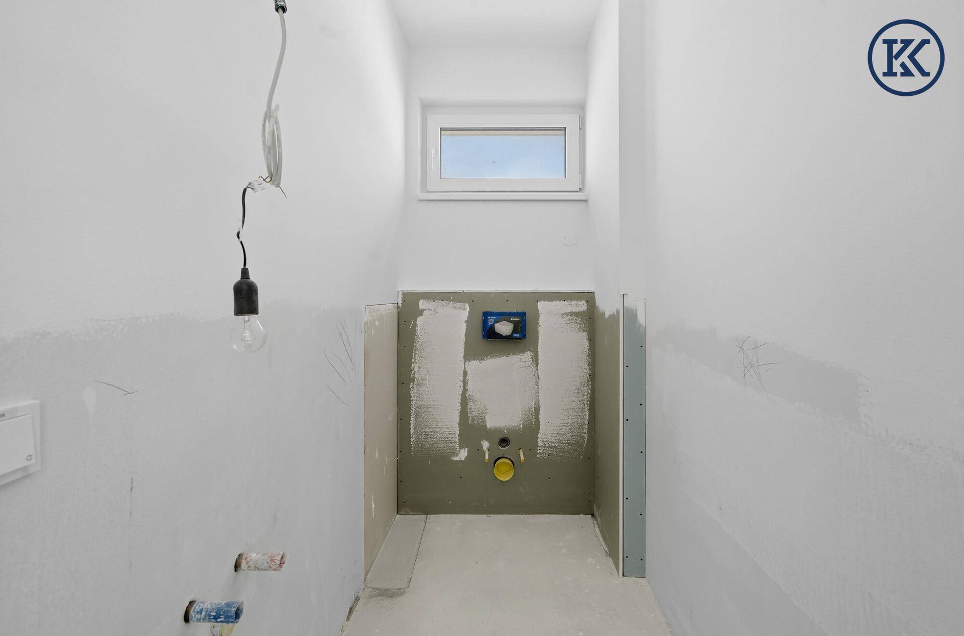Gäste-WC im Rohbau mit vorbereiteter Wandmontage für die Toilette und einem kleinen Fenster.