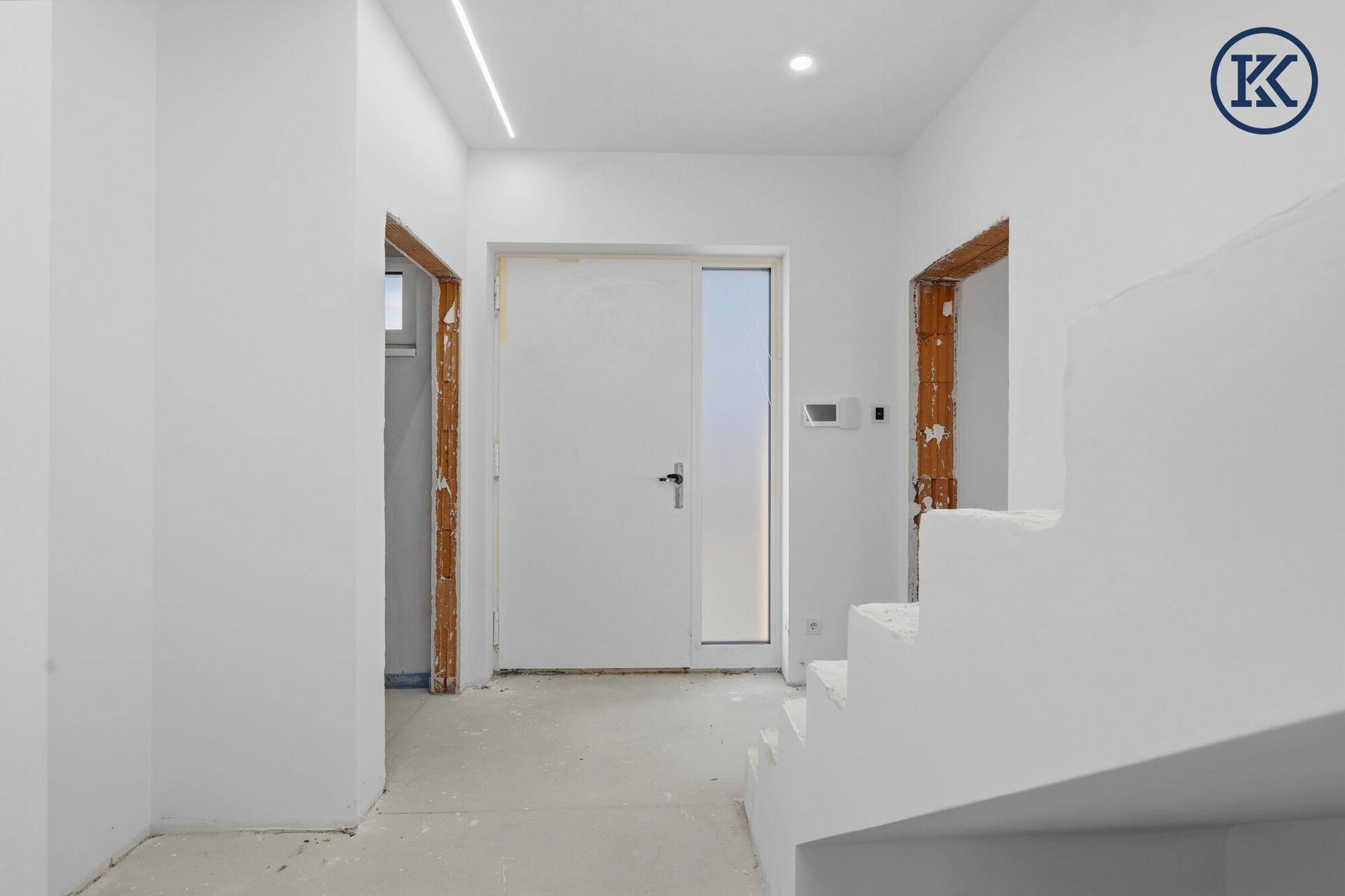 Heller Eingangsbereich im Rohbau mit Treppenaufgang und moderner Deckenbeleuchtung.