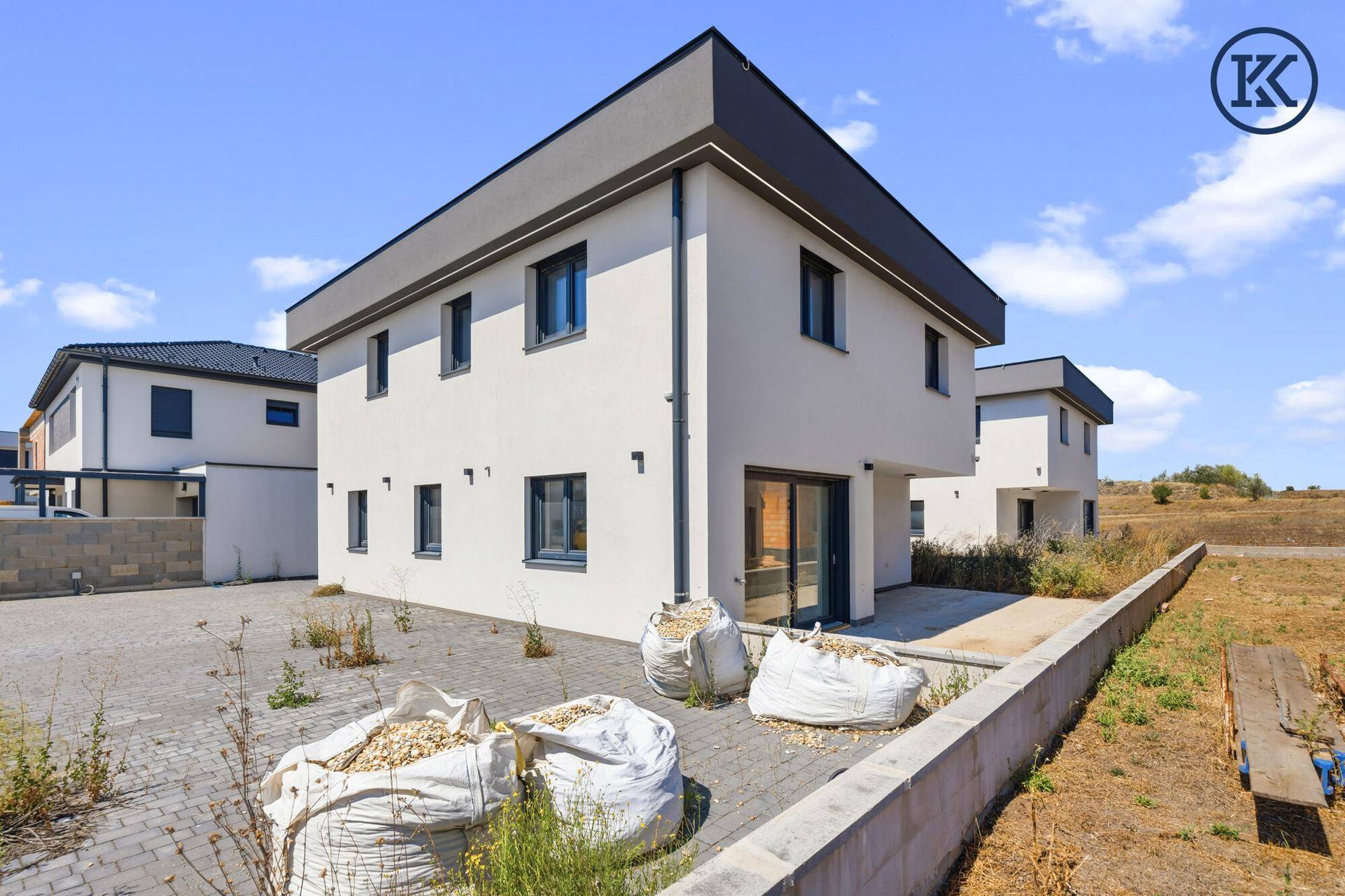 Neubau-Doppelhaushälfte mit gepflastertem Bereich und angrenzendem unbebautem Grundstück.