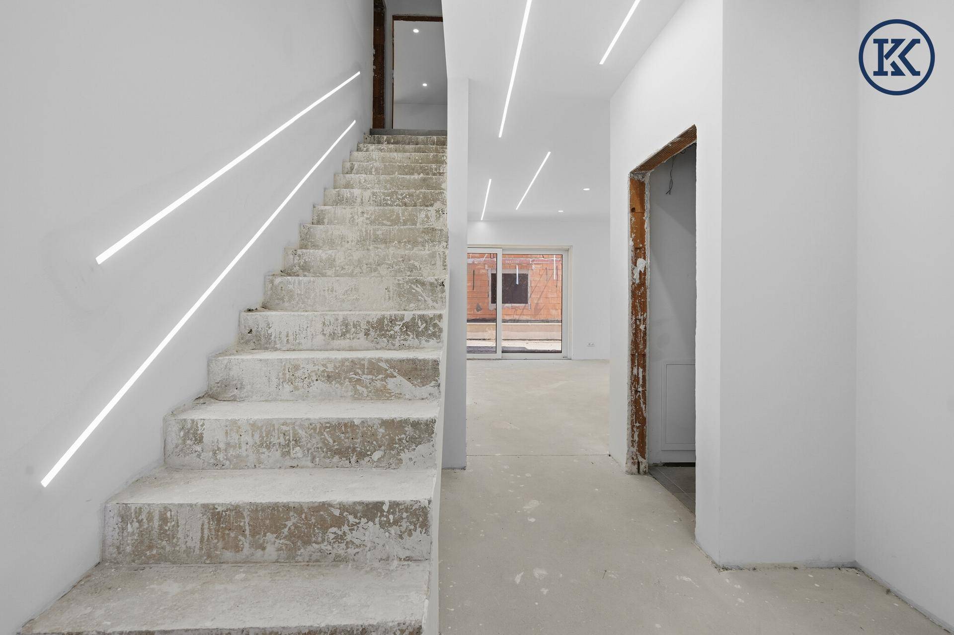 Treppenaufgang im Rohbau mit integrierter Deckenbeleuchtung und Blick in den Wohnbereich.