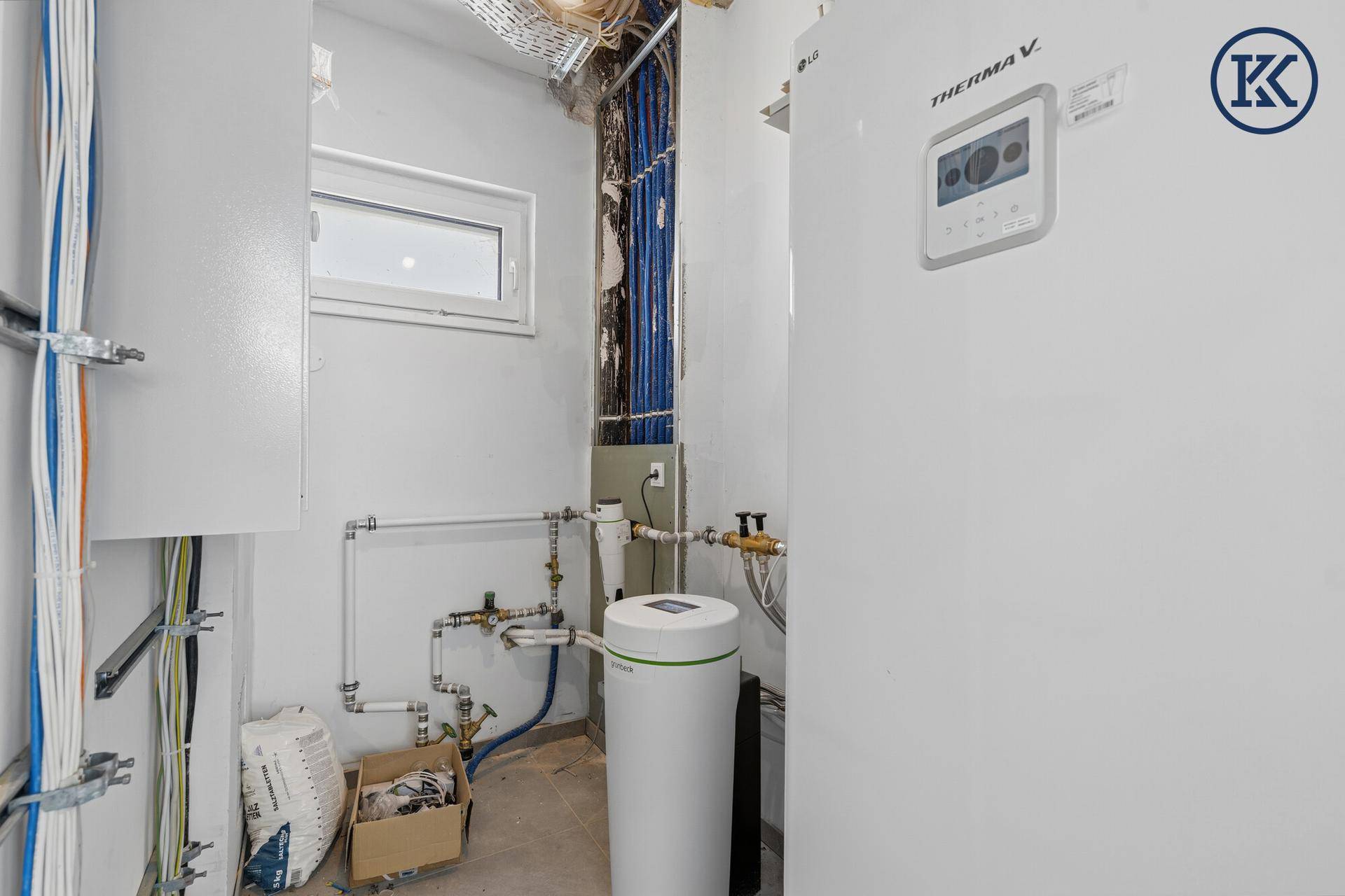 Technikraum mit Wärmepumpe, Wasserinstallationen und elektrischen Leitungen.