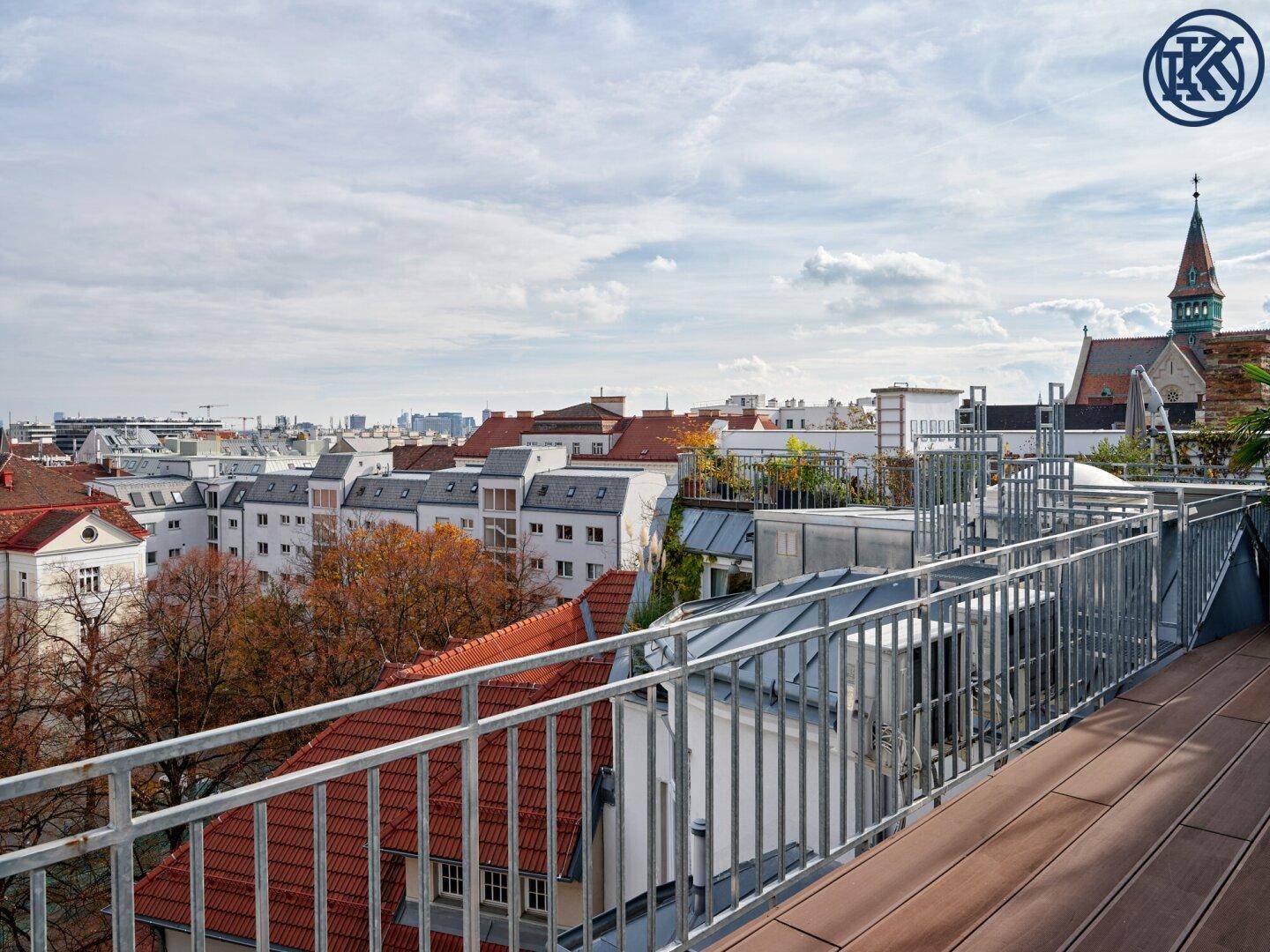 Panoramische Dachterrasse mit Holzboden und weitem Blick über die Dächer der Stadt und eine Kirche.