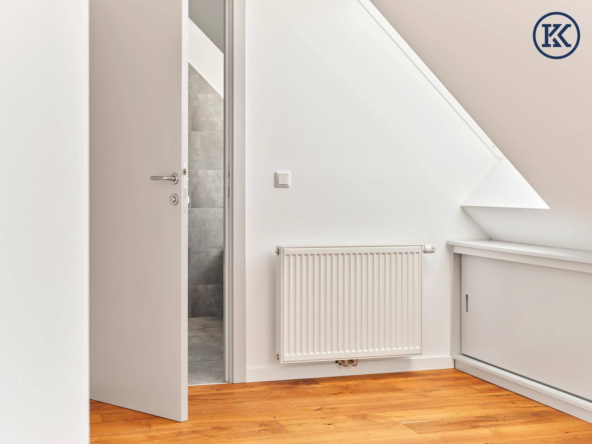 Türöffnung zu einem modernen Badezimmer, sichtbar ein Heizkörper und Holzboden im Vordergrund.