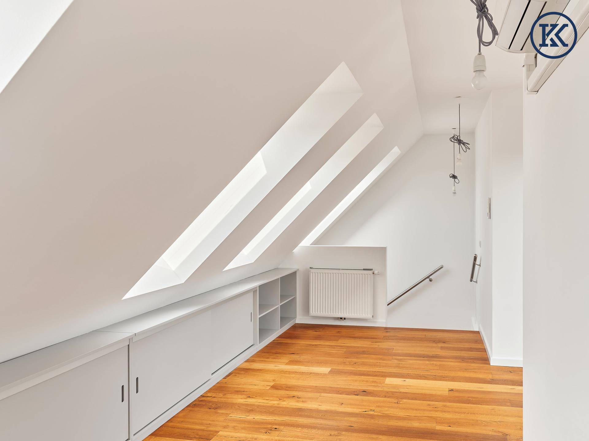 Lichtdurchflutetes Dachzimmer mit Holzboden, Dachschrägen, Einbauschränken und großen Dachfenstern.