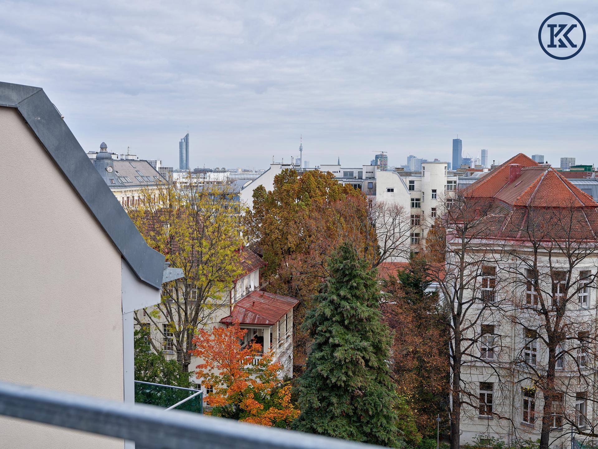 Panoramablick über die Stadt mit herbstlichen Bäumen und markanten Gebäuden unter bewölktem Himmel.