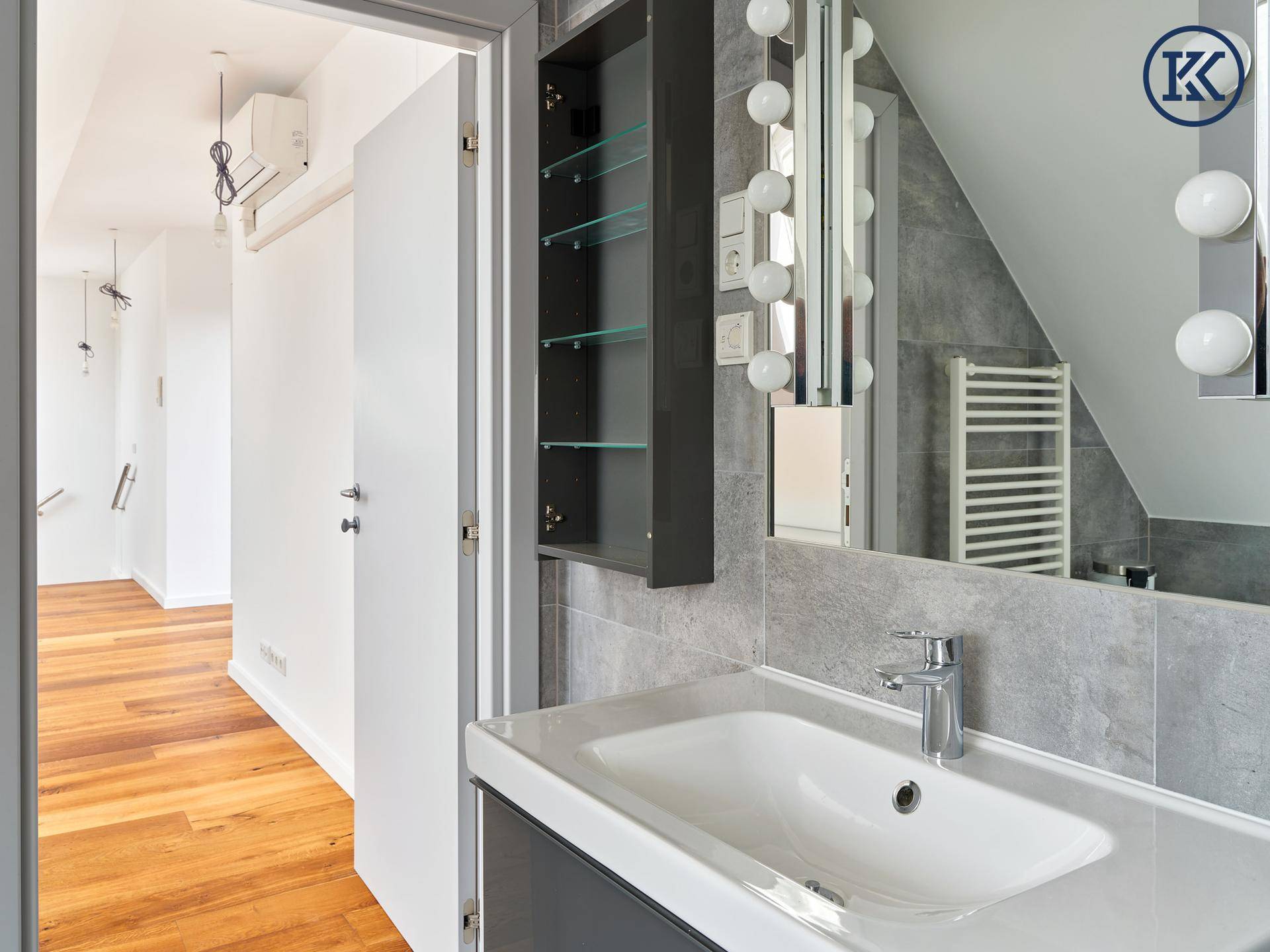 Modernes Badezimmer mit Waschtisch, großem Spiegelschrank und Blick in den angrenzenden Flur.