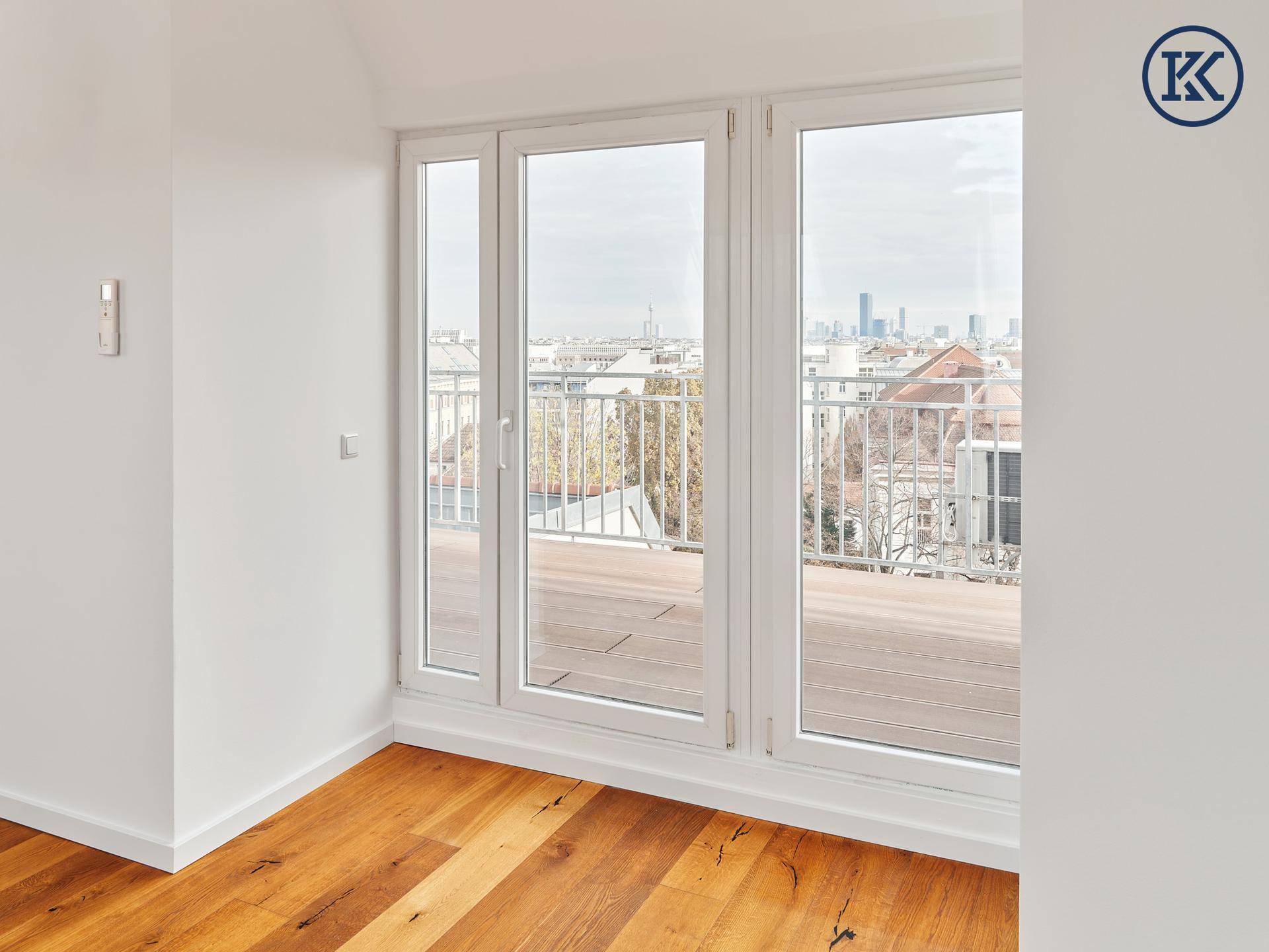 Große Fensterfront mit Zugang zu einem Außenbereich, bietet weiten Blick über die Stadt.