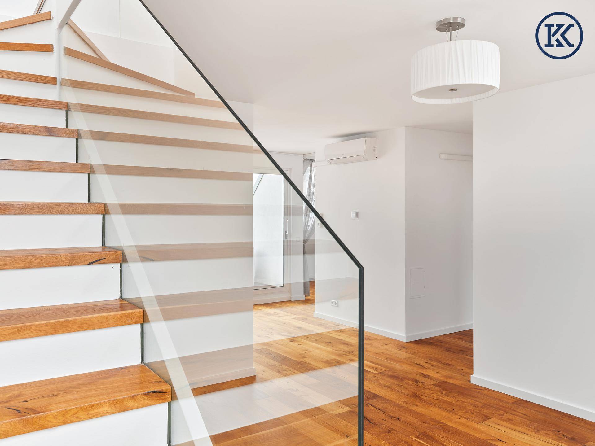 Moderne Holztreppe mit Glasgeländer verbindet die Etagen in einem hellen Flur.