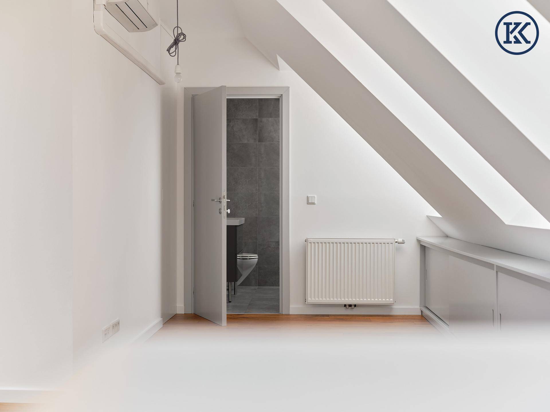 Geräumiges Dachgeschosszimmer mit Holzboden, Heizkörper und Zugang zu einem Badezimmer.