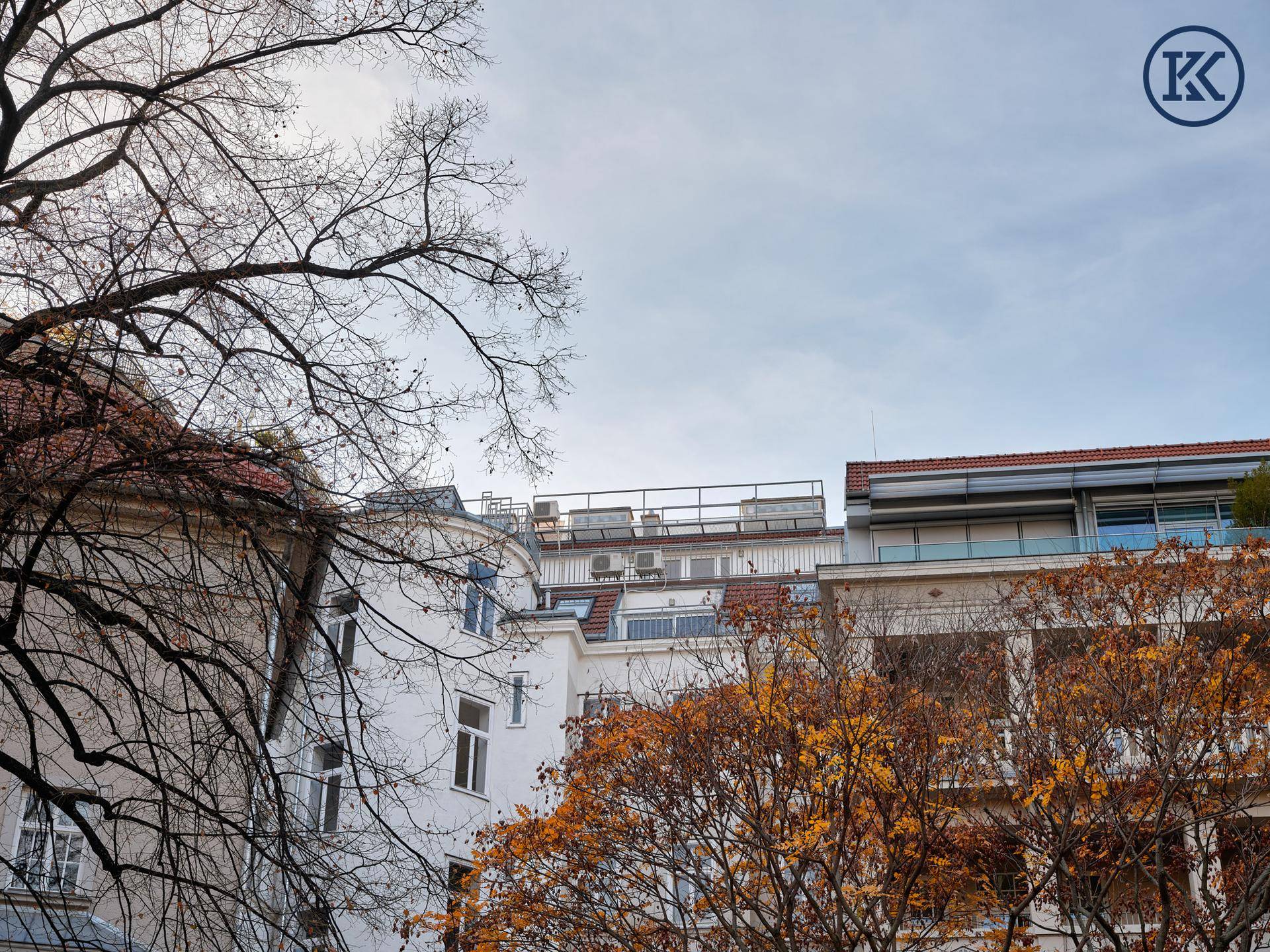 Blick auf die umliegenden Gebäude und herbstliche Bäume unter bewölktem Himmel.