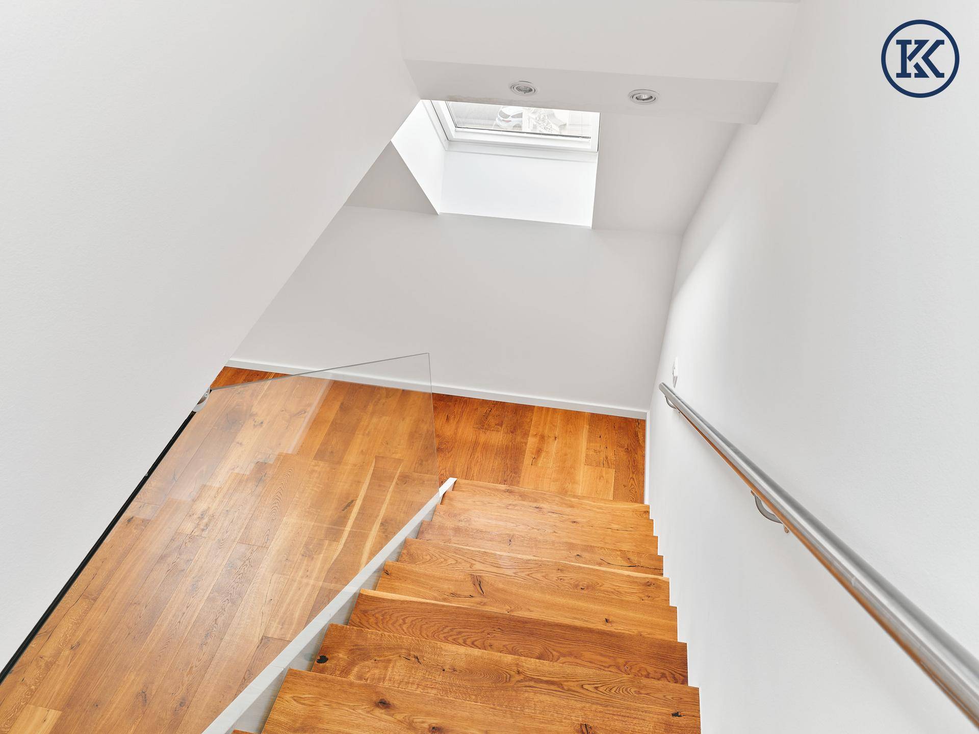 Heller Treppenaufgang mit Holzdielen und einem Oberlicht, das Tageslicht spendet.