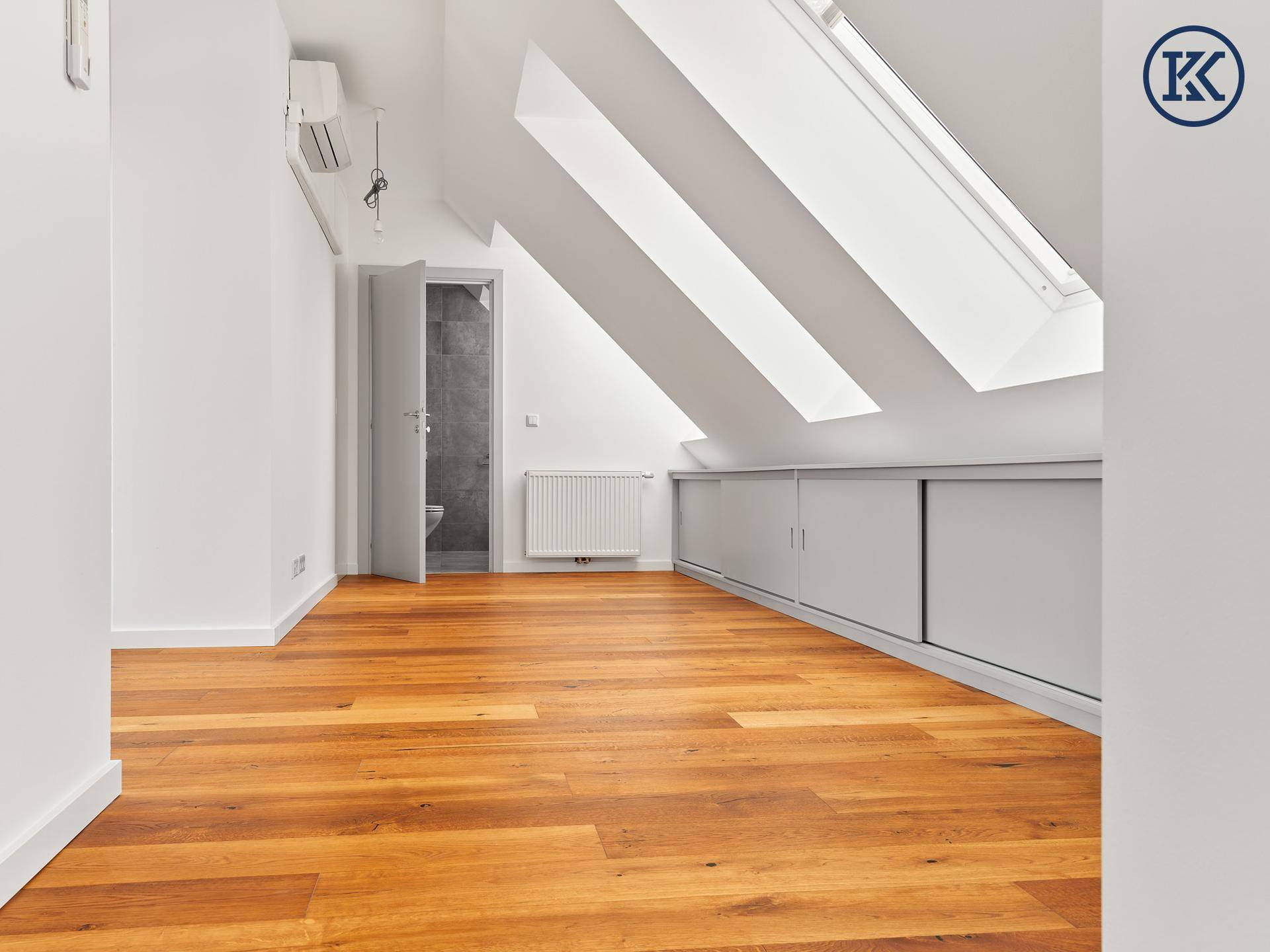 Helles Dachgeschosszimmer mit Holzboden, Dachfenstern und integrierten Schränken.