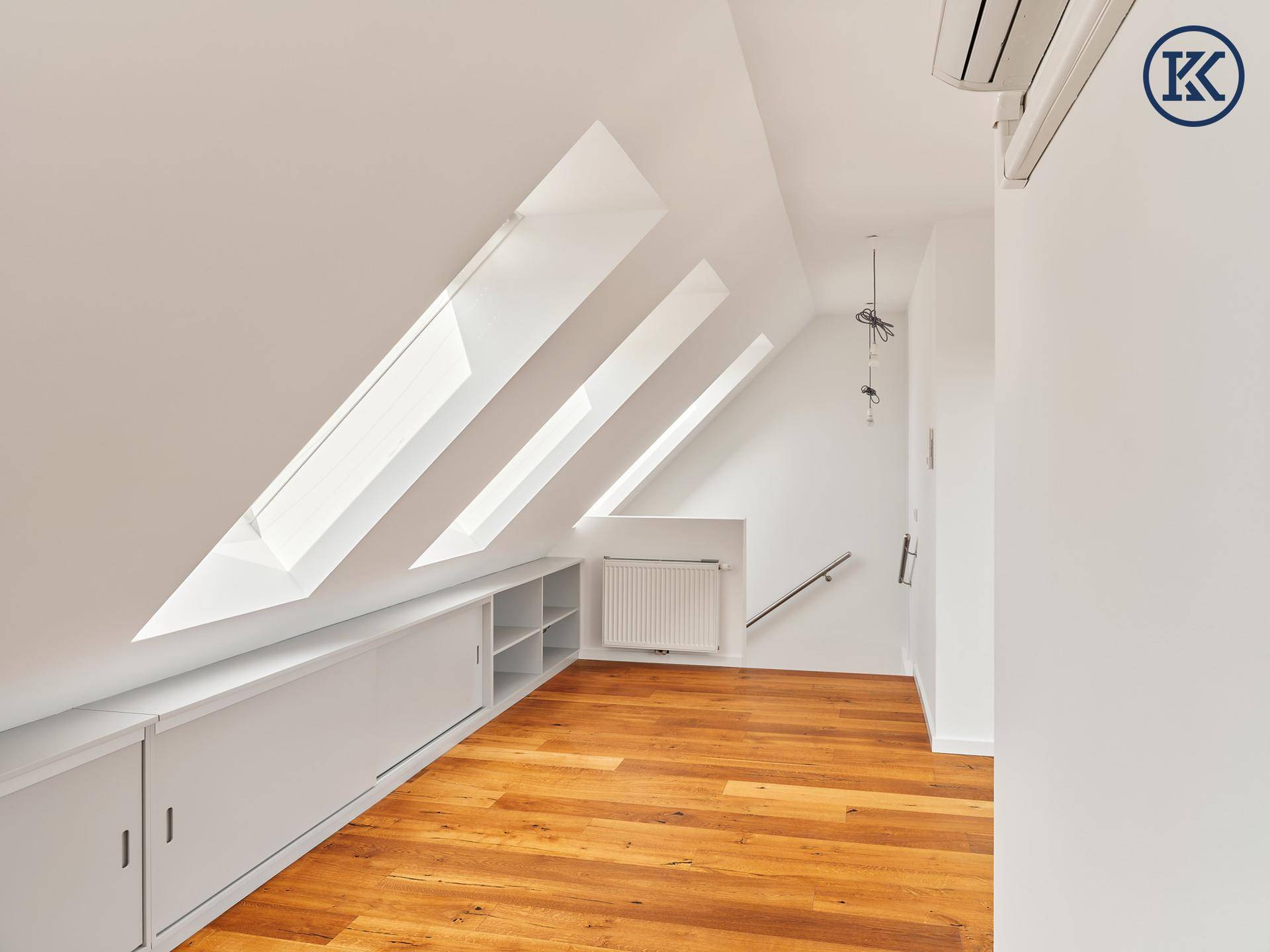 Heller Dachbodenraum mit schrägen Wänden, Dachfenstern, Holzboden und integrierten Stauschränken.