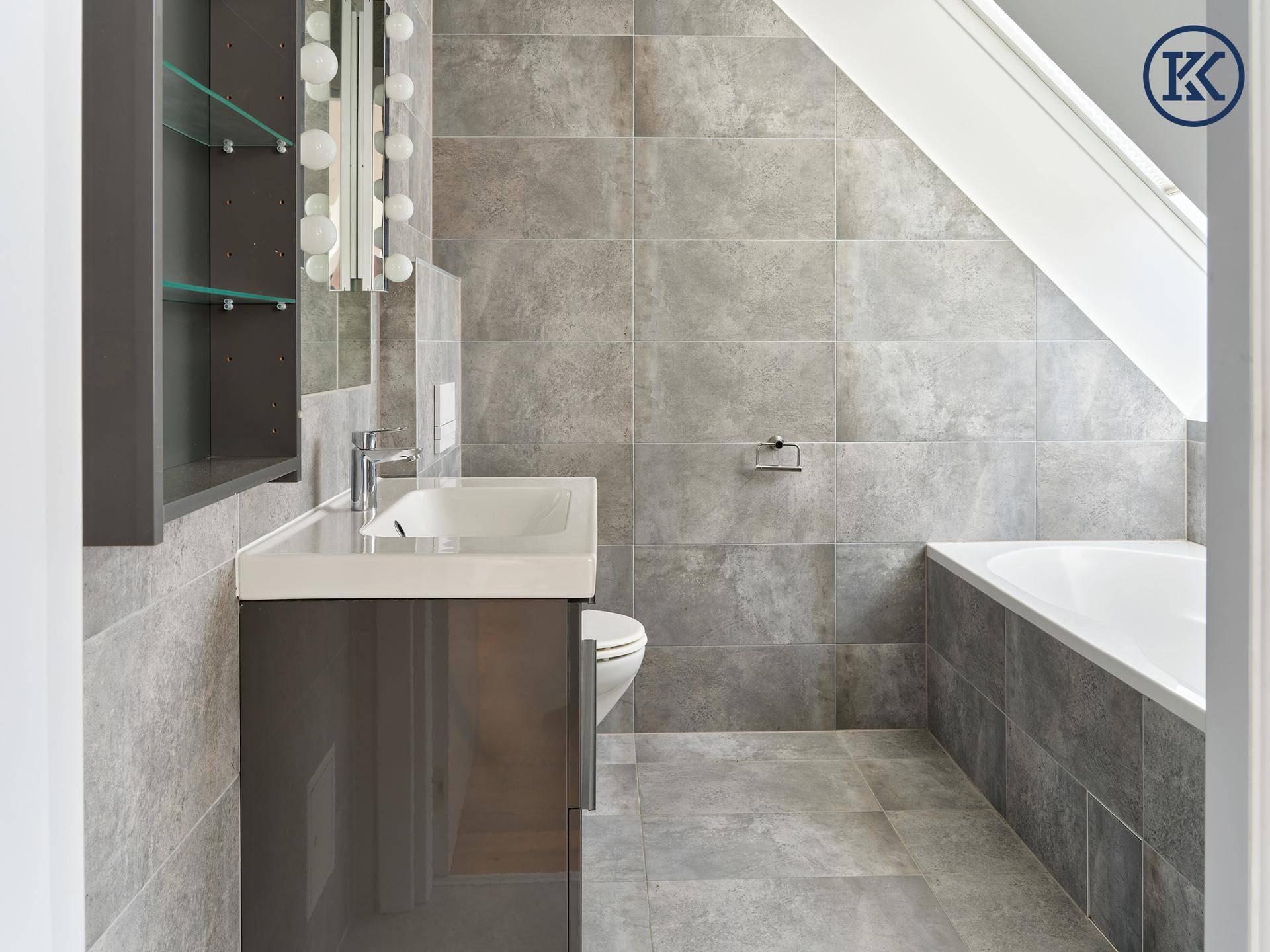 Modernes Badezimmer mit grauen Großformatfliesen, Badewanne und Dachfenster.