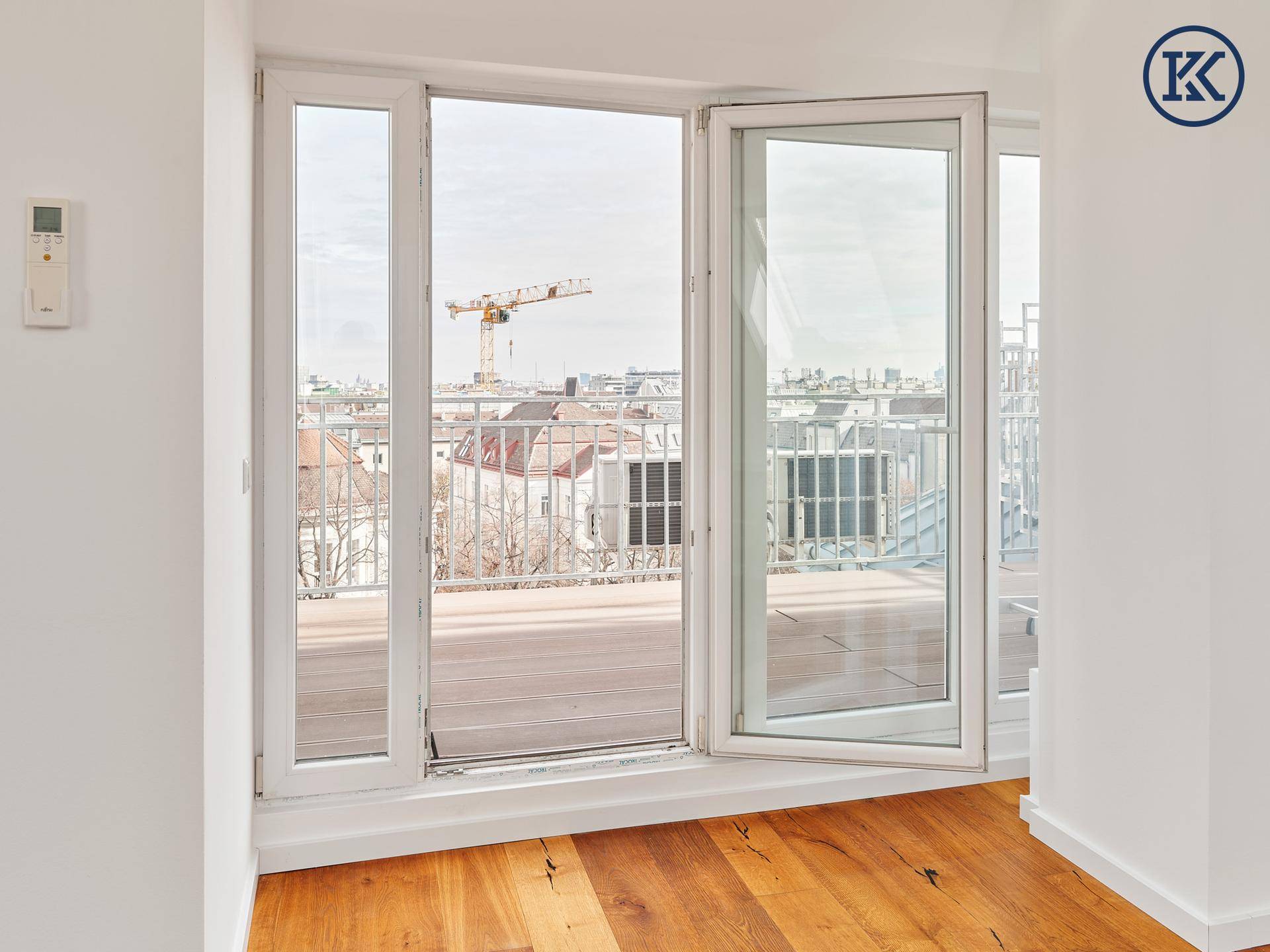 Offenes Fenster in einem hellen Raum mit Holzboden und Blick auf die Stadt und einen Kran.