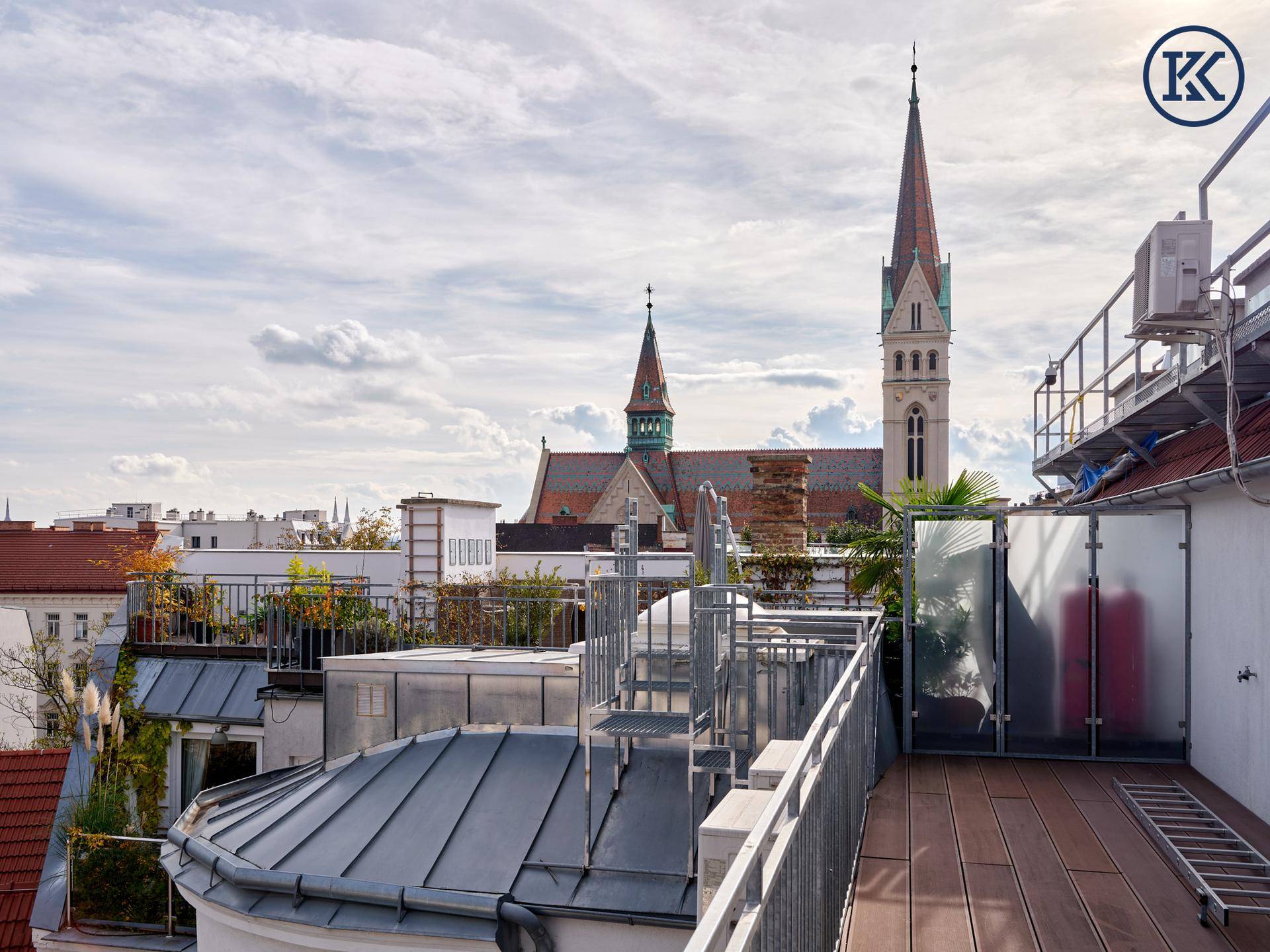 Dachterrasse mit Panoramablick auf die Stadt, inklusive einer historischen Kirche und moderner Architektur.