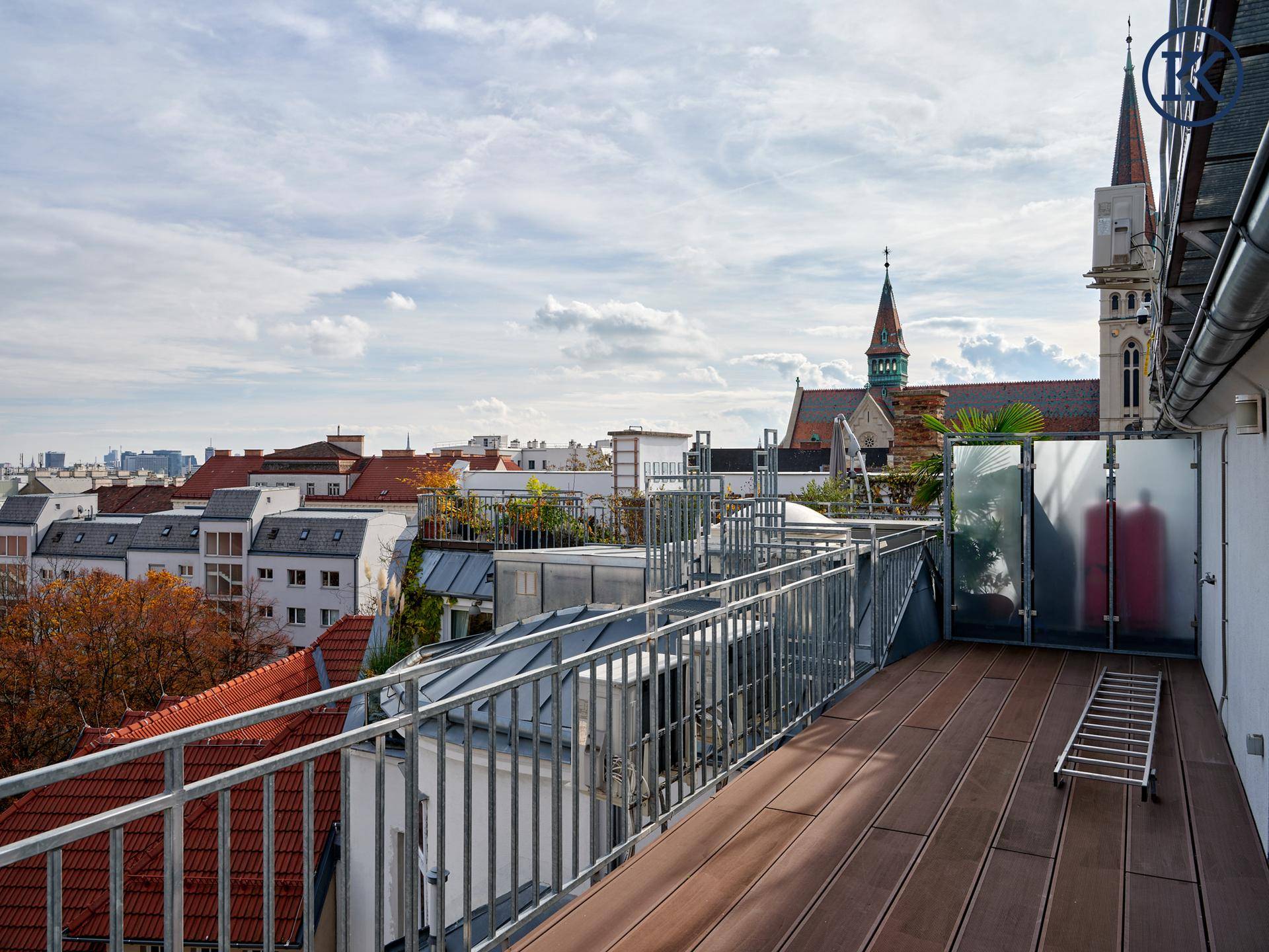 Geräumige Dachterrasse mit Holzboden und weitem Blick auf die Stadt und eine Kirche.