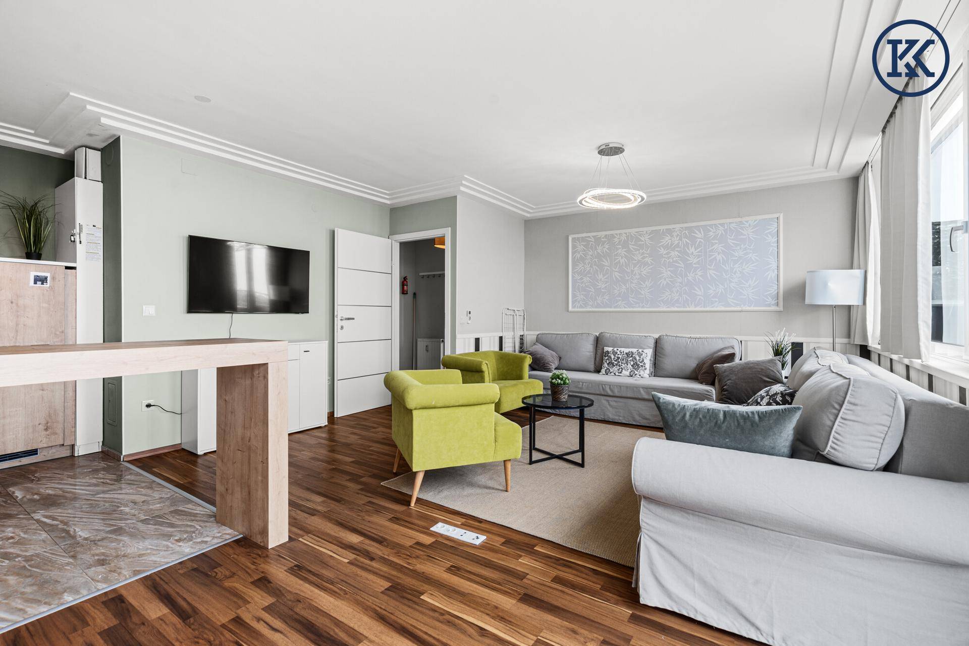 Geräumiges Wohnzimmer mit Holzboden, Fernseher an der Wand und Zugang zu weiteren Räumen.