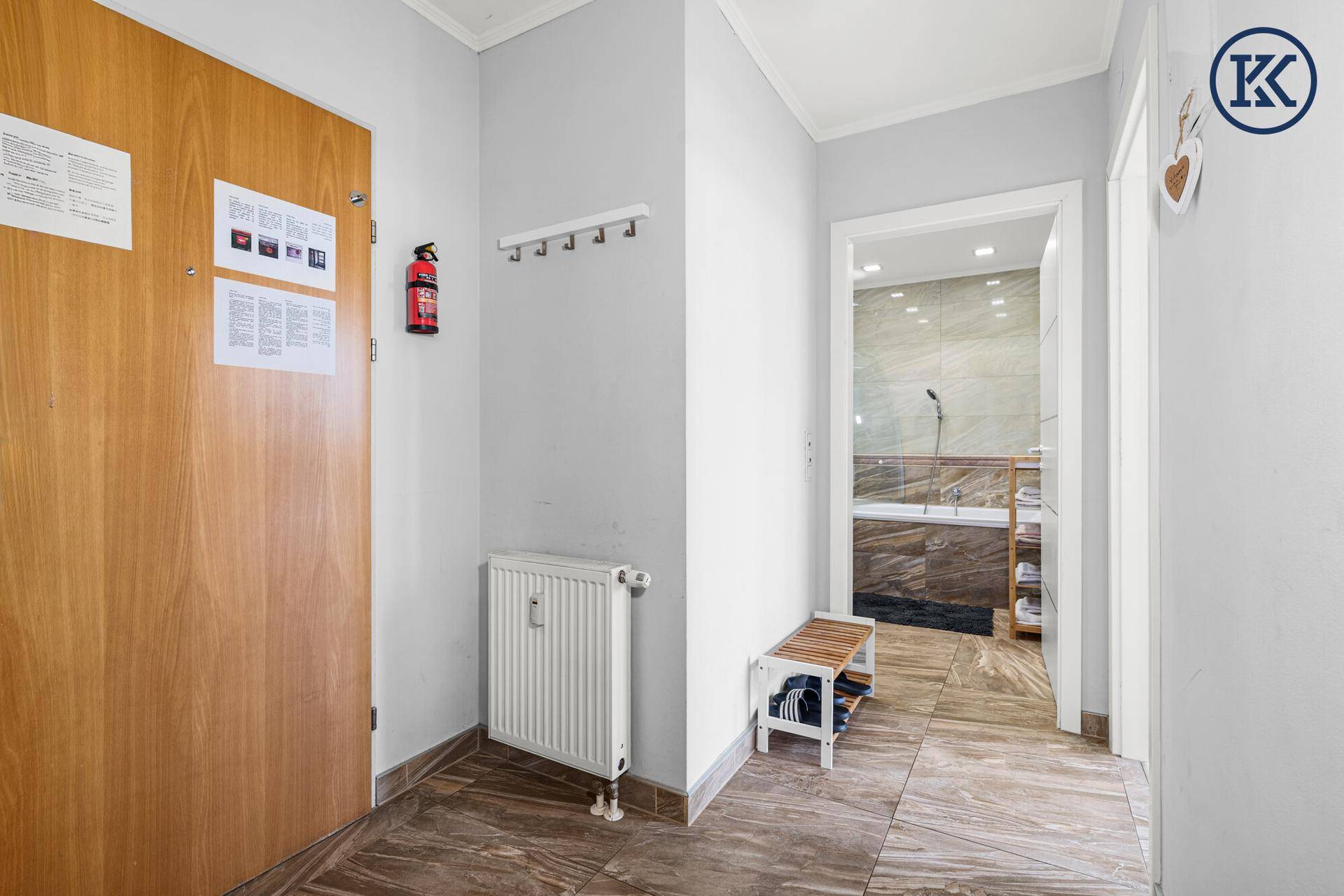 Heller Flur mit Holztür, Garderobe und Zugang zum Badezimmer.