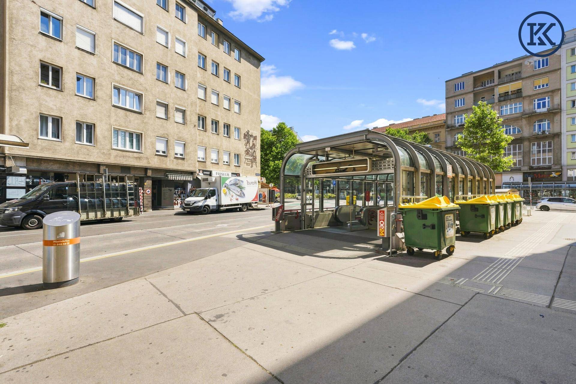 Straßenansicht mit U-Bahn-Eingang und umliegenden Wohngebäuden unter blauem Himmel.
