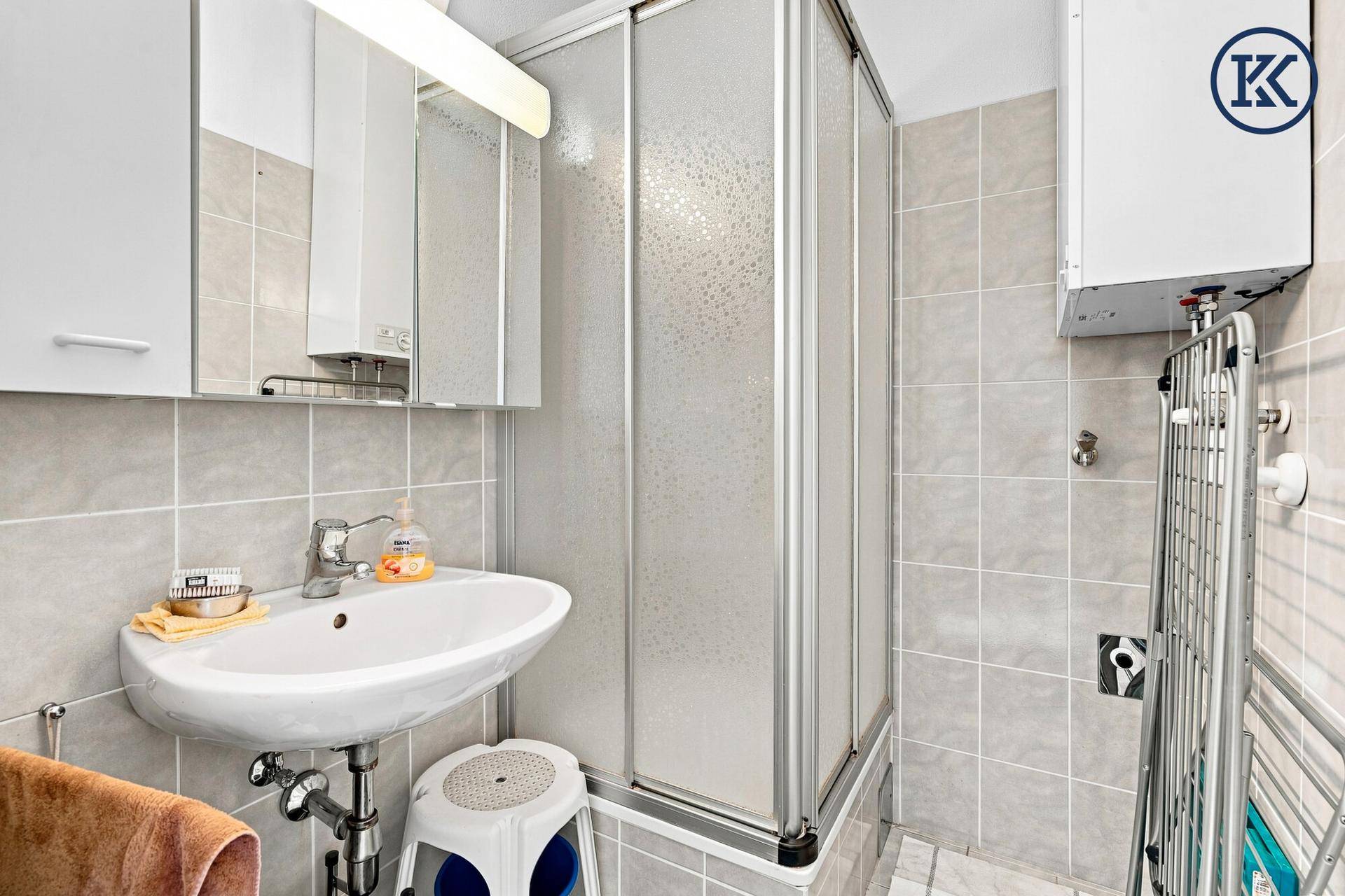 Kleines Badezimmer mit Dusche, Waschbecken und hellgrauen Fliesen.