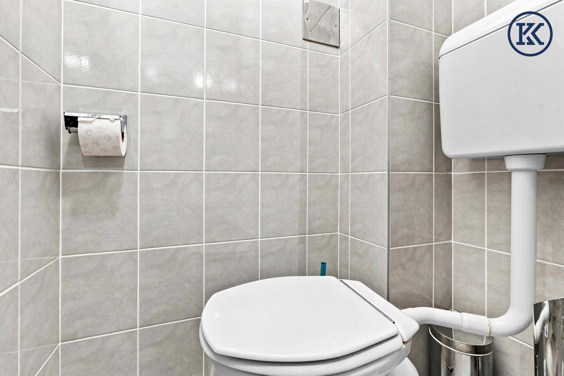 Separates WC mit hellgrauen Wandfliesen und Standard-Toilette.