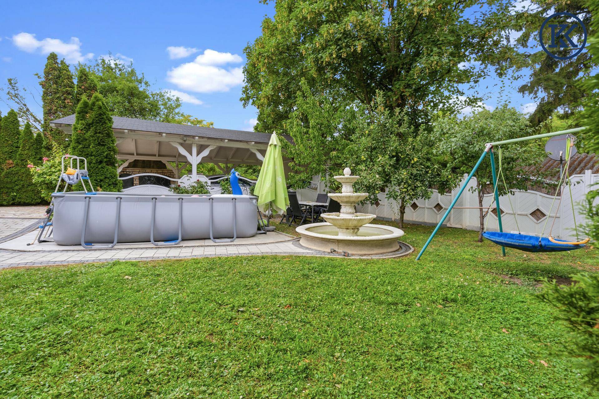 Großer Garten mit Aufstellpool, Springbrunnen und Schaukel für Kinder.