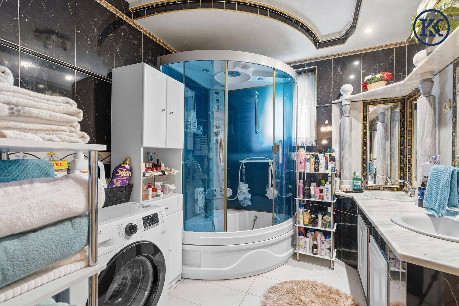 Geräumiges Badezimmer mit Duschkabine, Waschmaschine und dunklen Marmorfliesen.